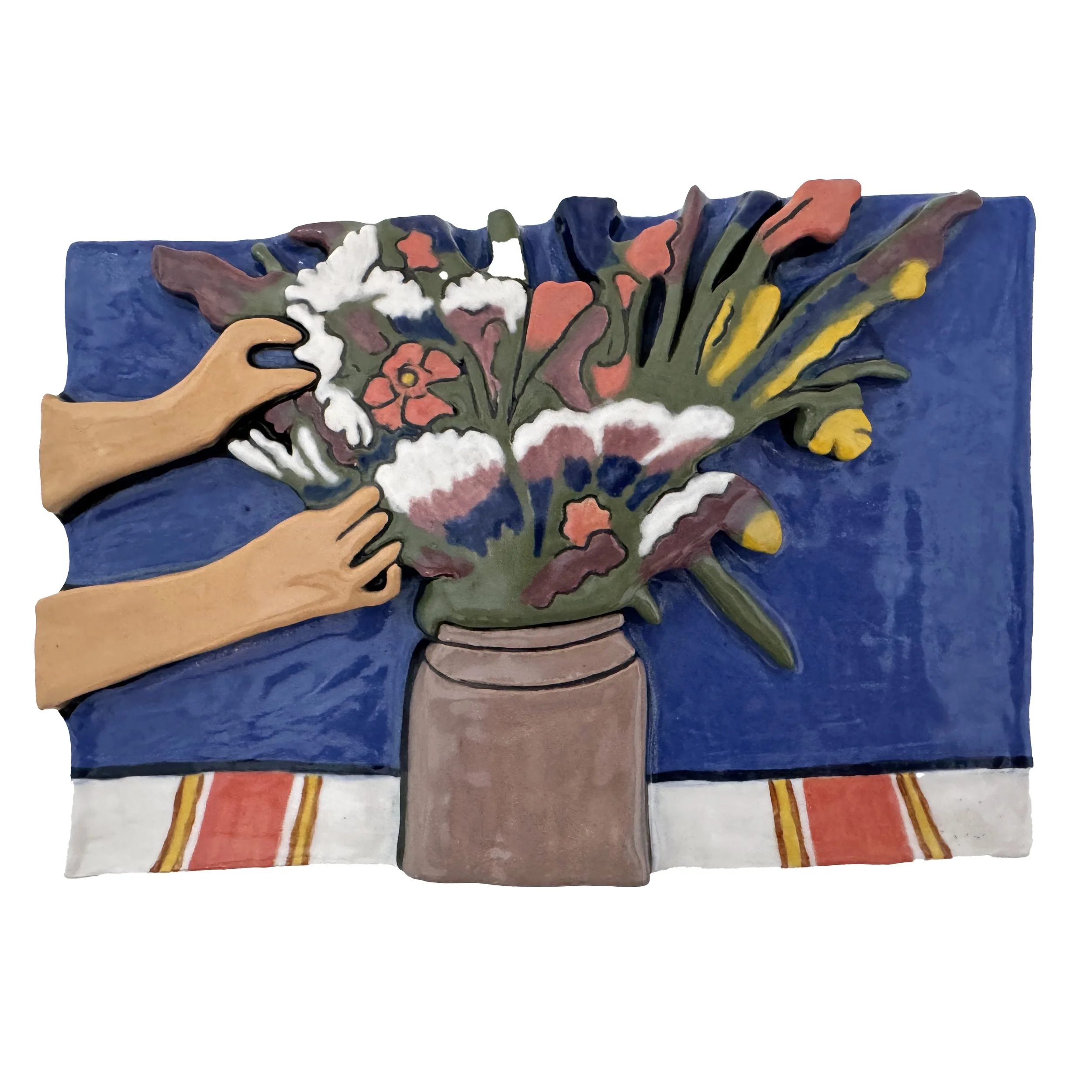 A painted, ceramic relief of a hand arranging a bouquet of colorful flowers in a vase on a table with a red and yellow striped cloth. The background is blue.