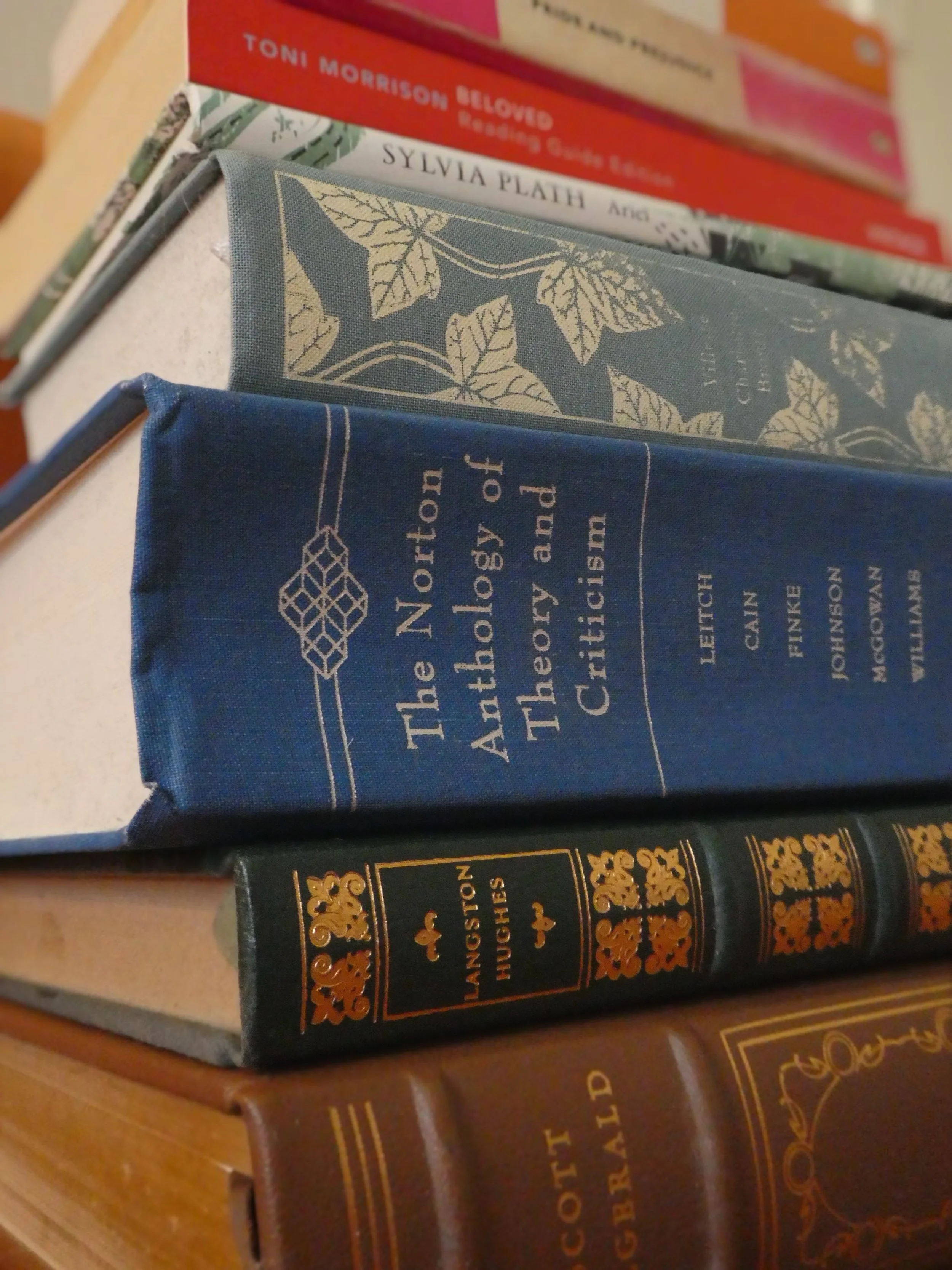 Stack of books. From top to bottom: 'Beloved' by Toni Morrison, 'Ariel' by Sylvia Plath, 'Villette' by Charlotte Bronte, 'The Norton Anthology of Theory and Criticism', Langston Hughes