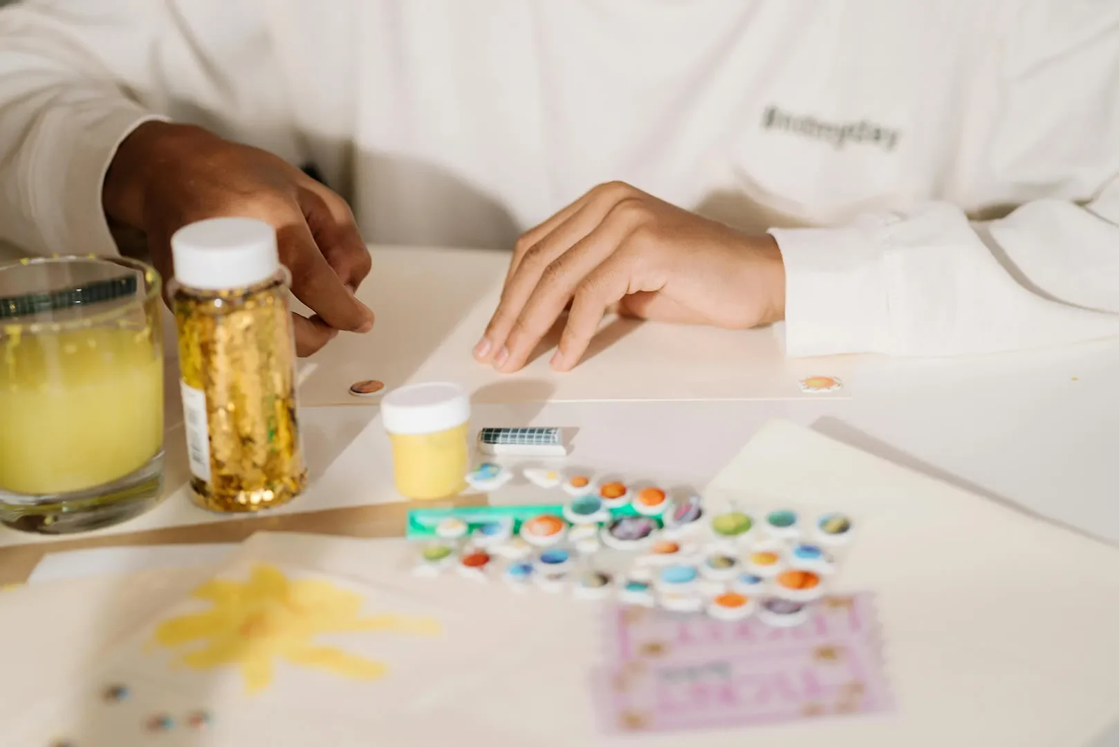 Art supplies on table, glitter, stickers, and paint with glass of water