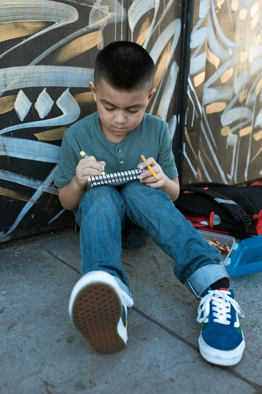 Child outside coloring with a crayon on spiral notepad.