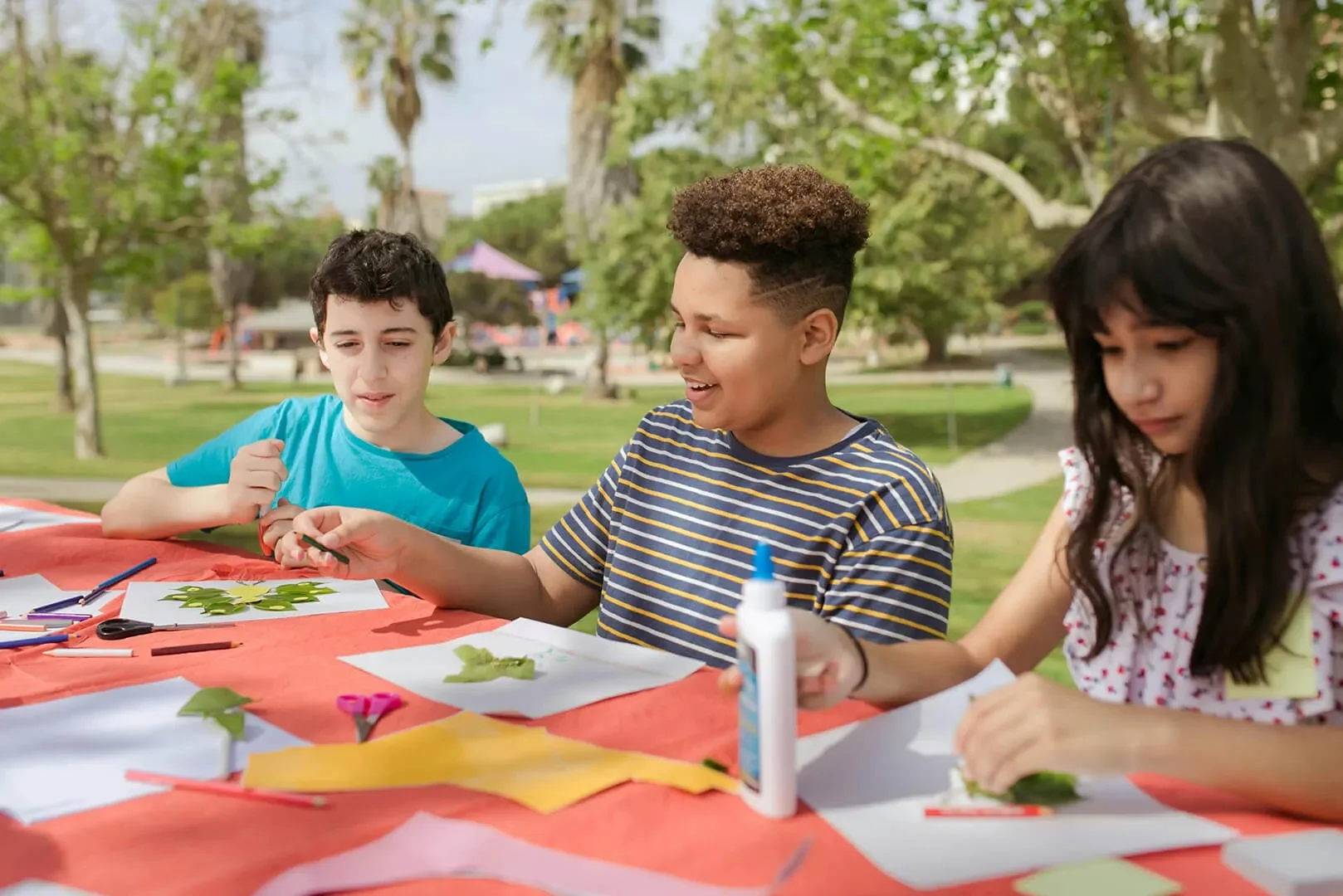 Group of children doing crafts in an outdoor park on a sunny day.