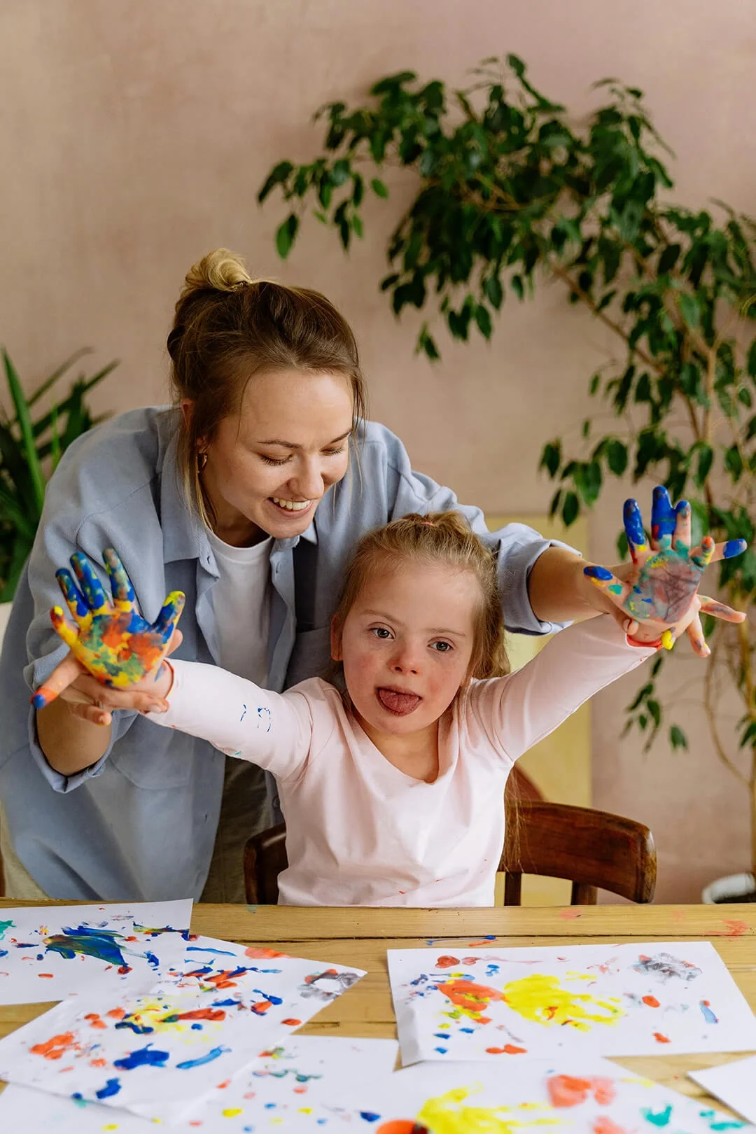Adult and child smiling during a paint activity, holding up hands covered in colorful paint.