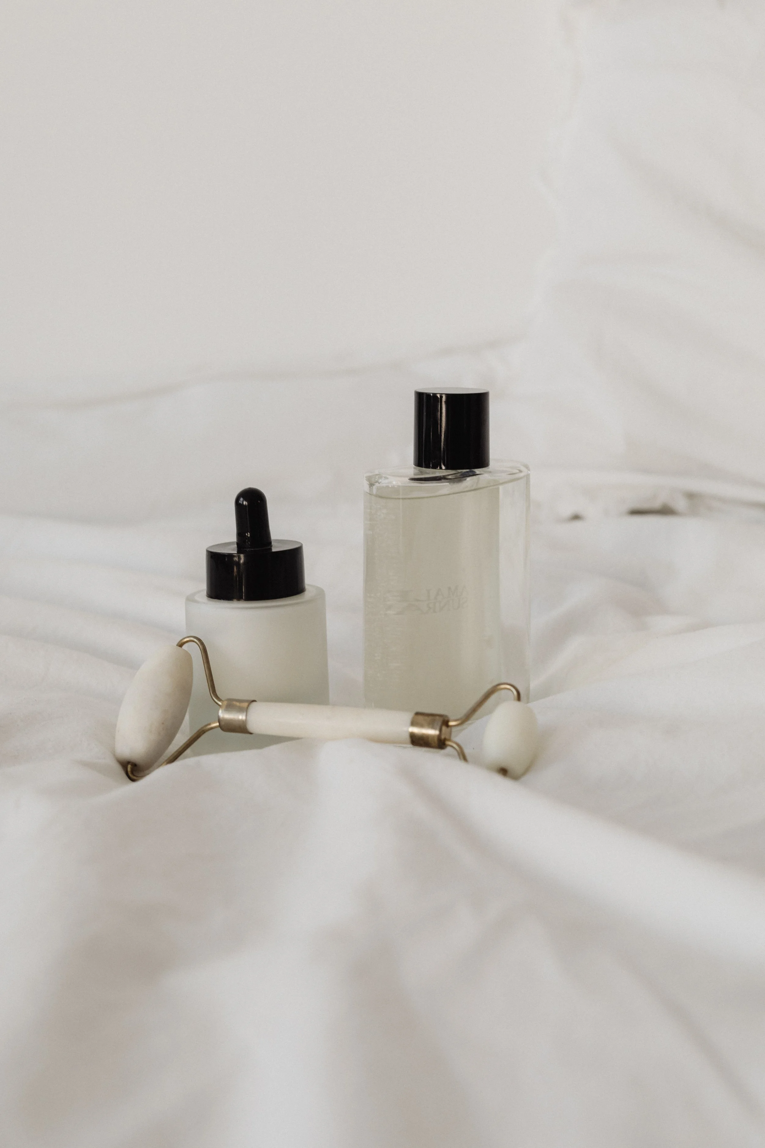 Skincare tools and bottles on a white bed.