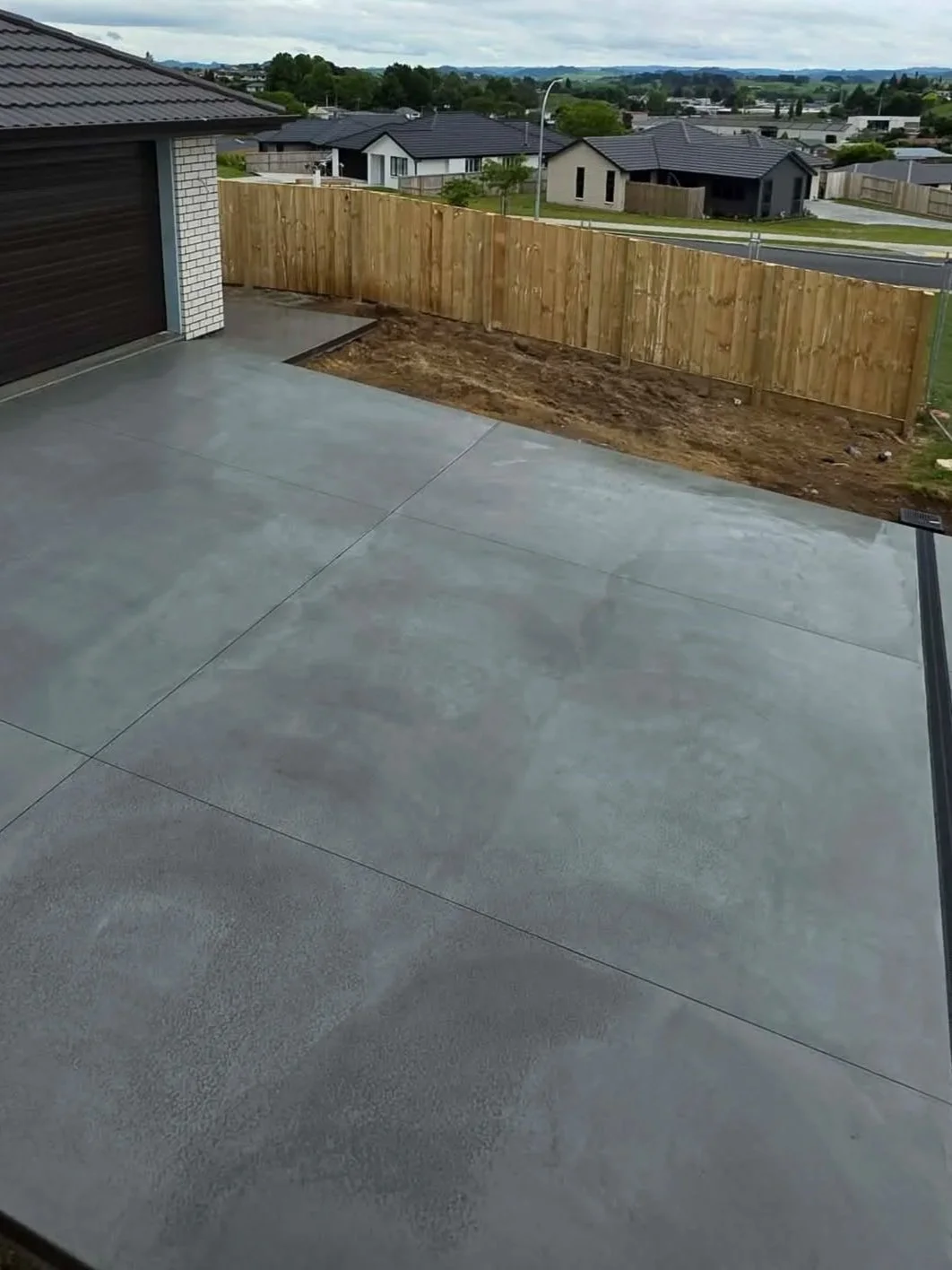 Newly finished concrete patio with a wooden fence in a suburban backyard.