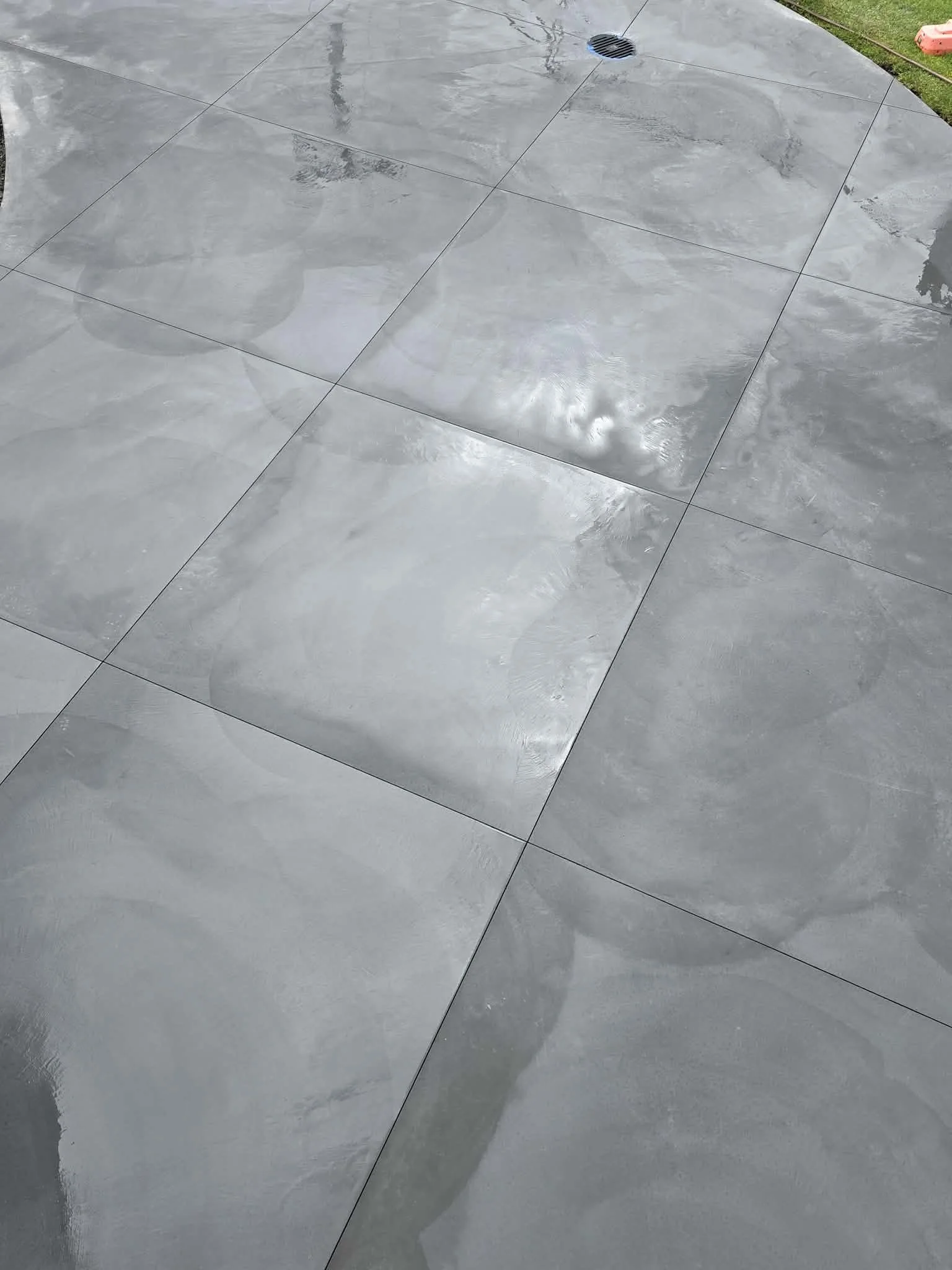 Wet gray tiled floor with a drain and reflections of the sky and surroundings.