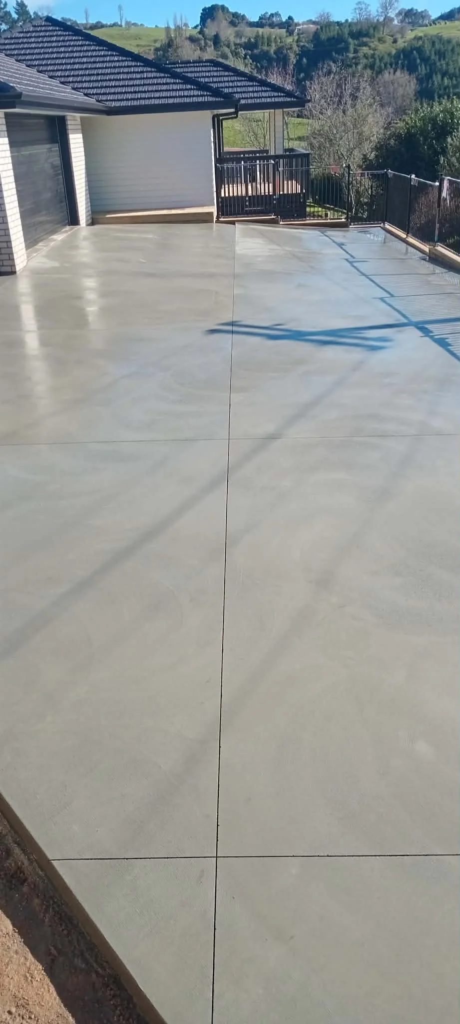 Freshly poured concrete patio in a backyard with a house, metal railing, and scenic hills in the background.