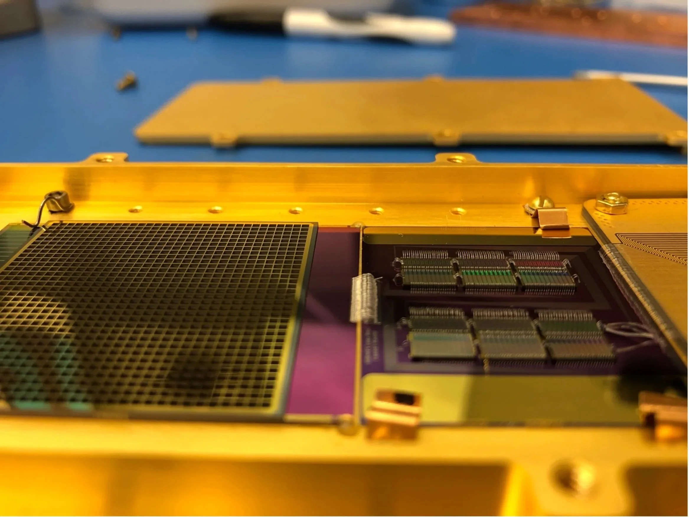 Close-up of a computer hardware circuit board with a gold-colored heatsink and green electronic components on a blue work surface.