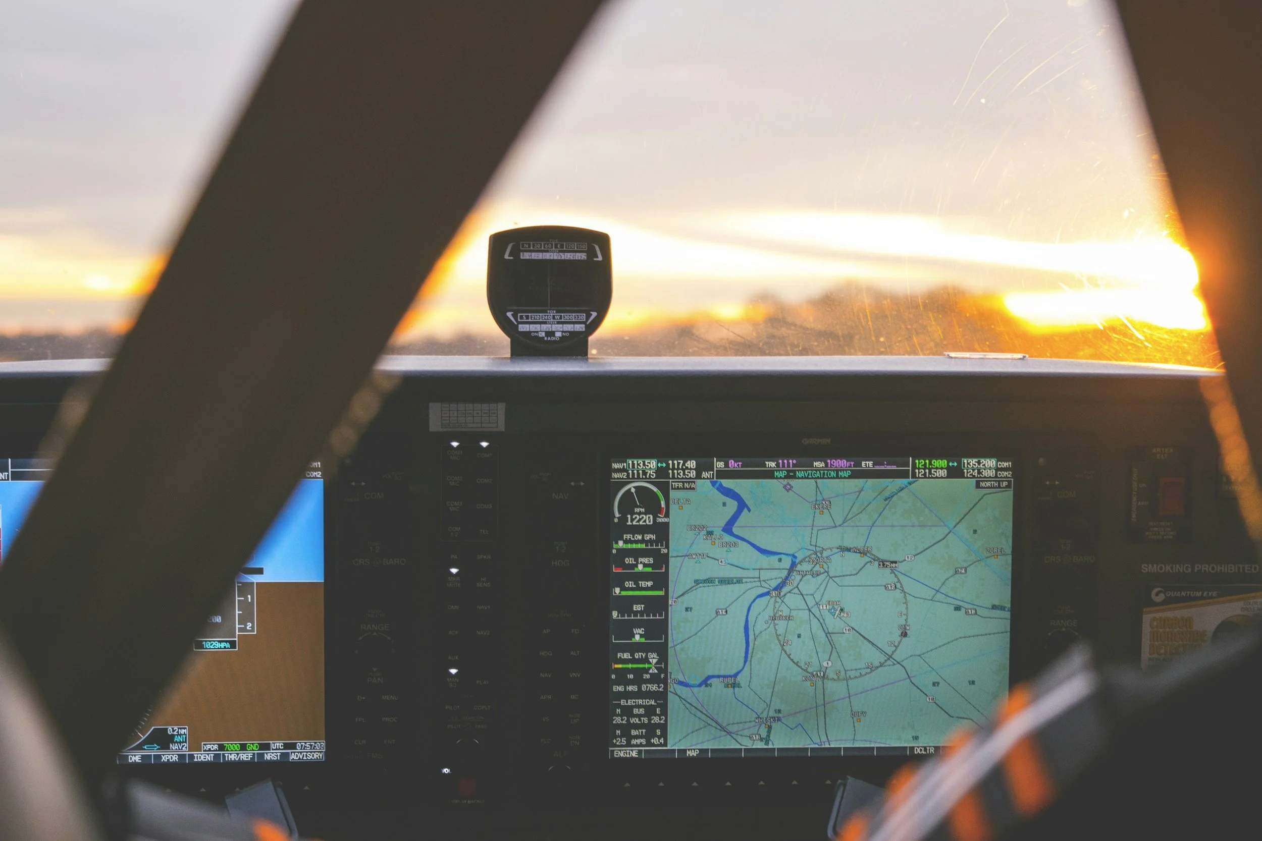 Cockpit of an airplane displaying navigation and instrument screens with a sunset view outside the window.