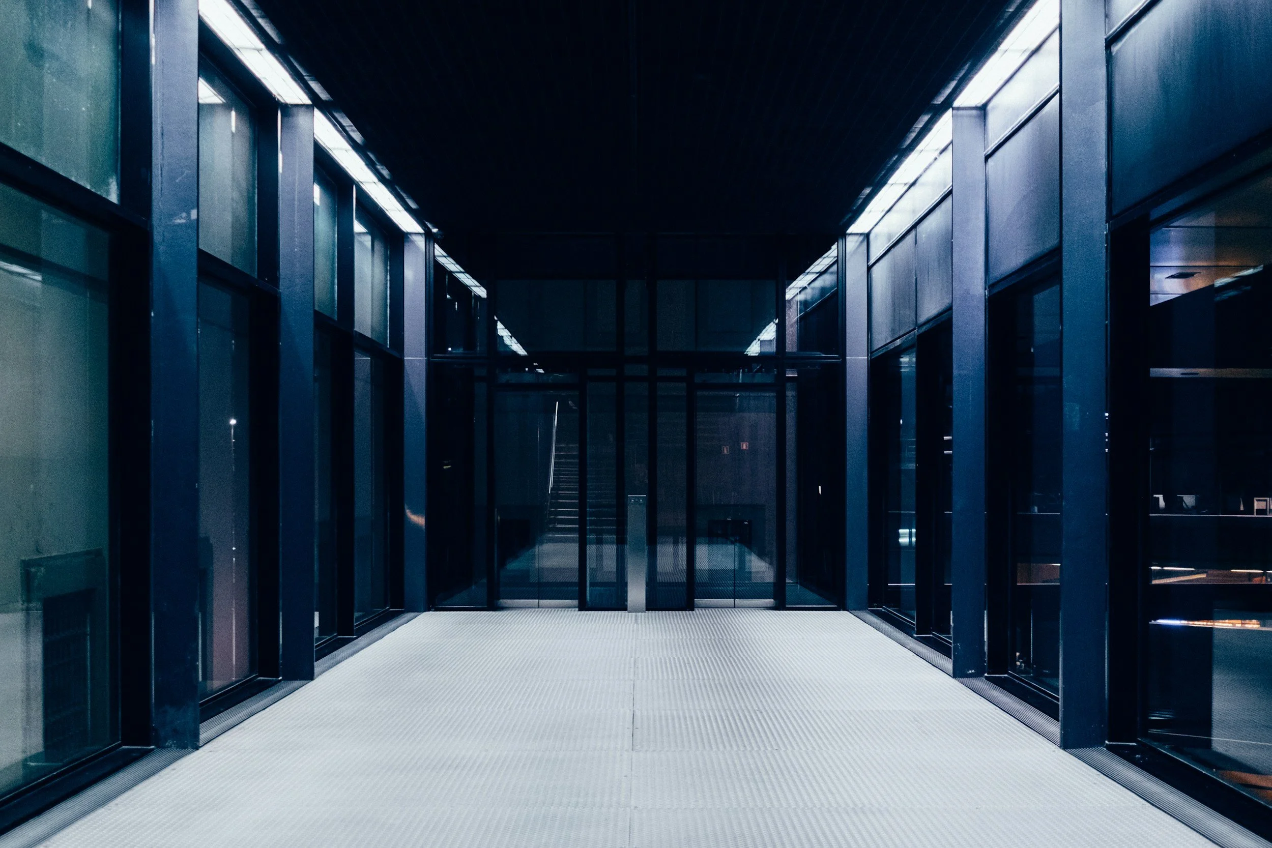 Empty modern glass corridor or walkway with black metal framing and reflective windows at night.