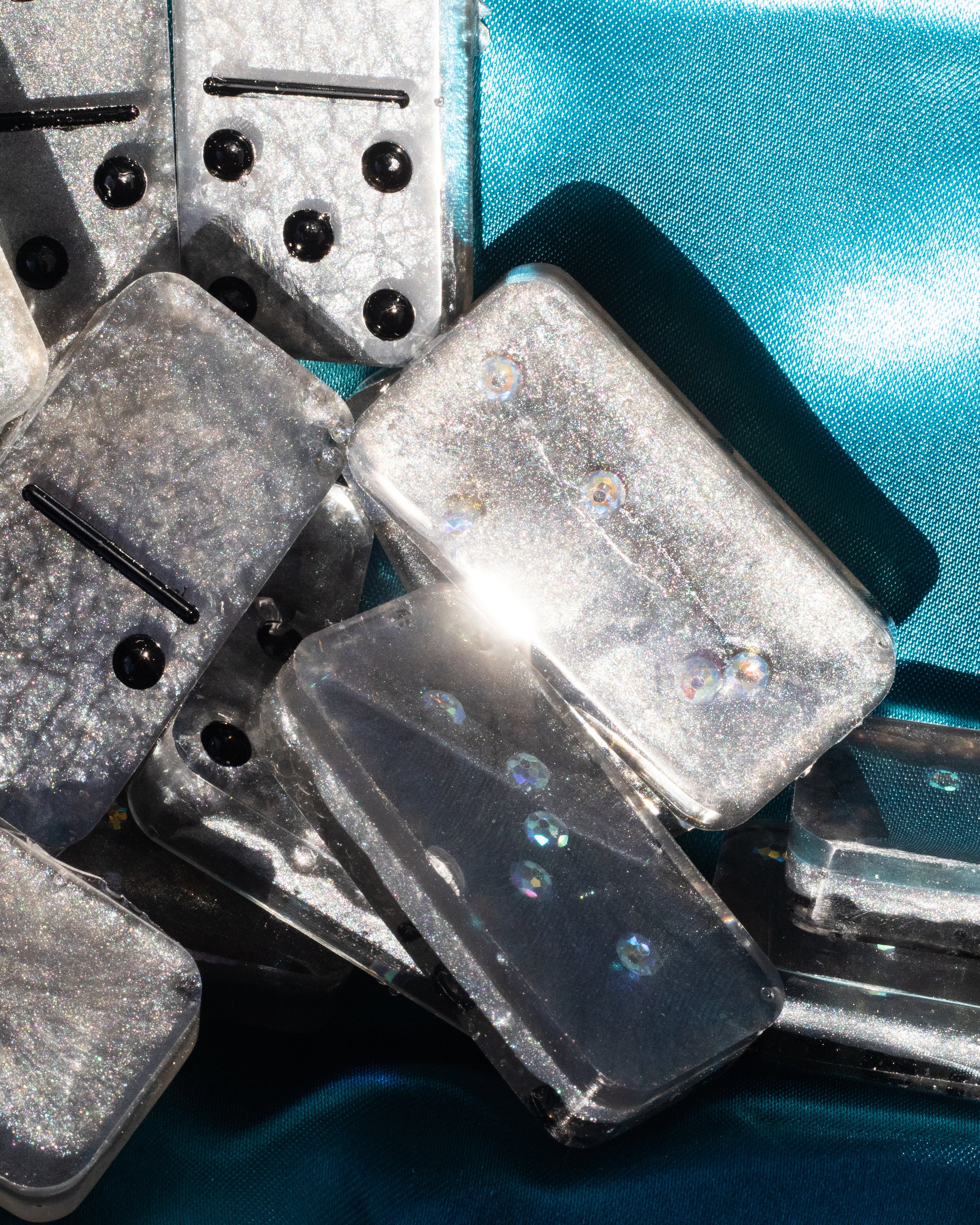 A collection of rectangular, glittery, glitter-filled transparent objects with black pins and a metal pin, placed on a blue fabric background, with light reflections on the surfaces.