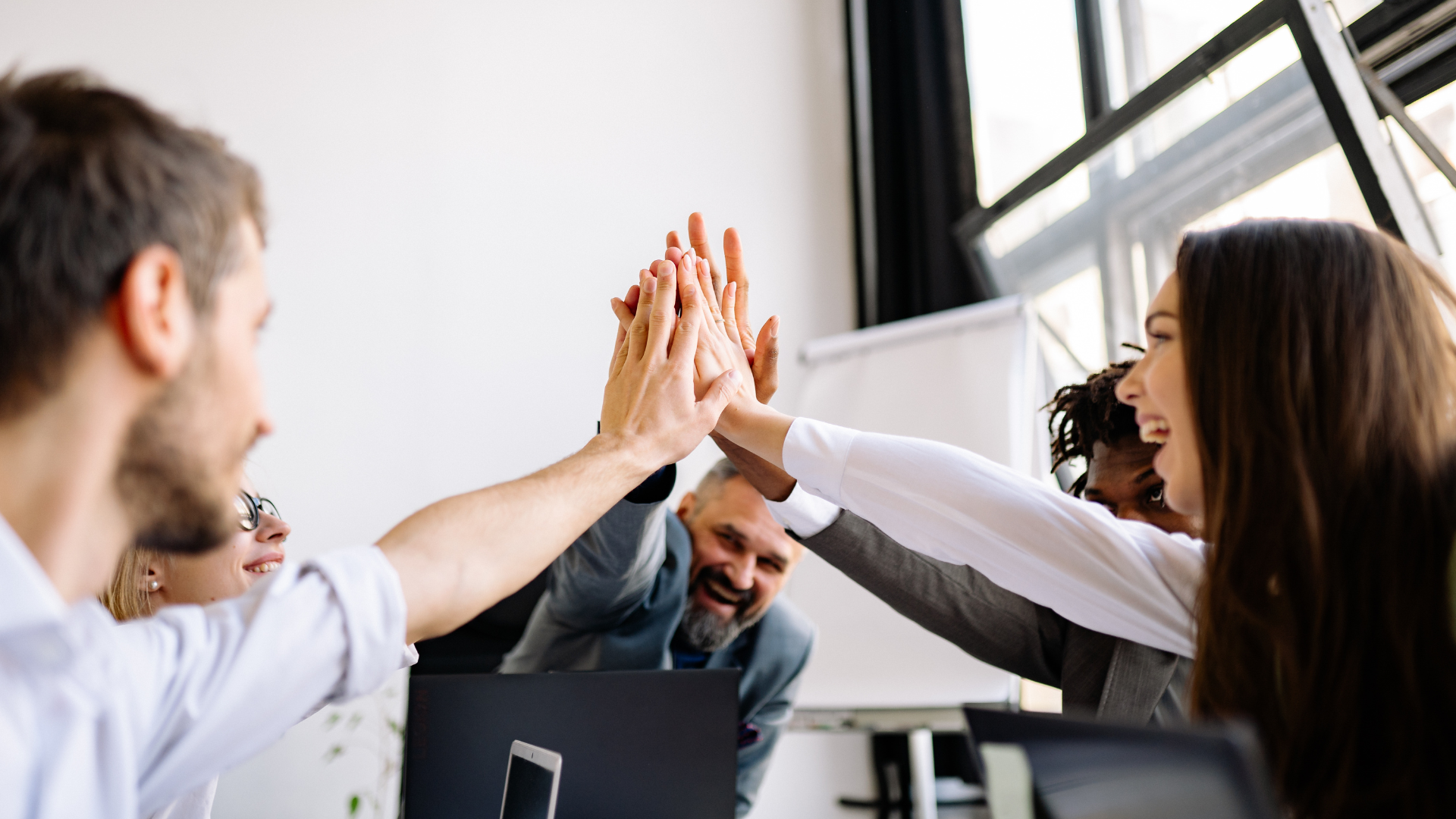 Team of diverse business people giving high five in a modern office meeting