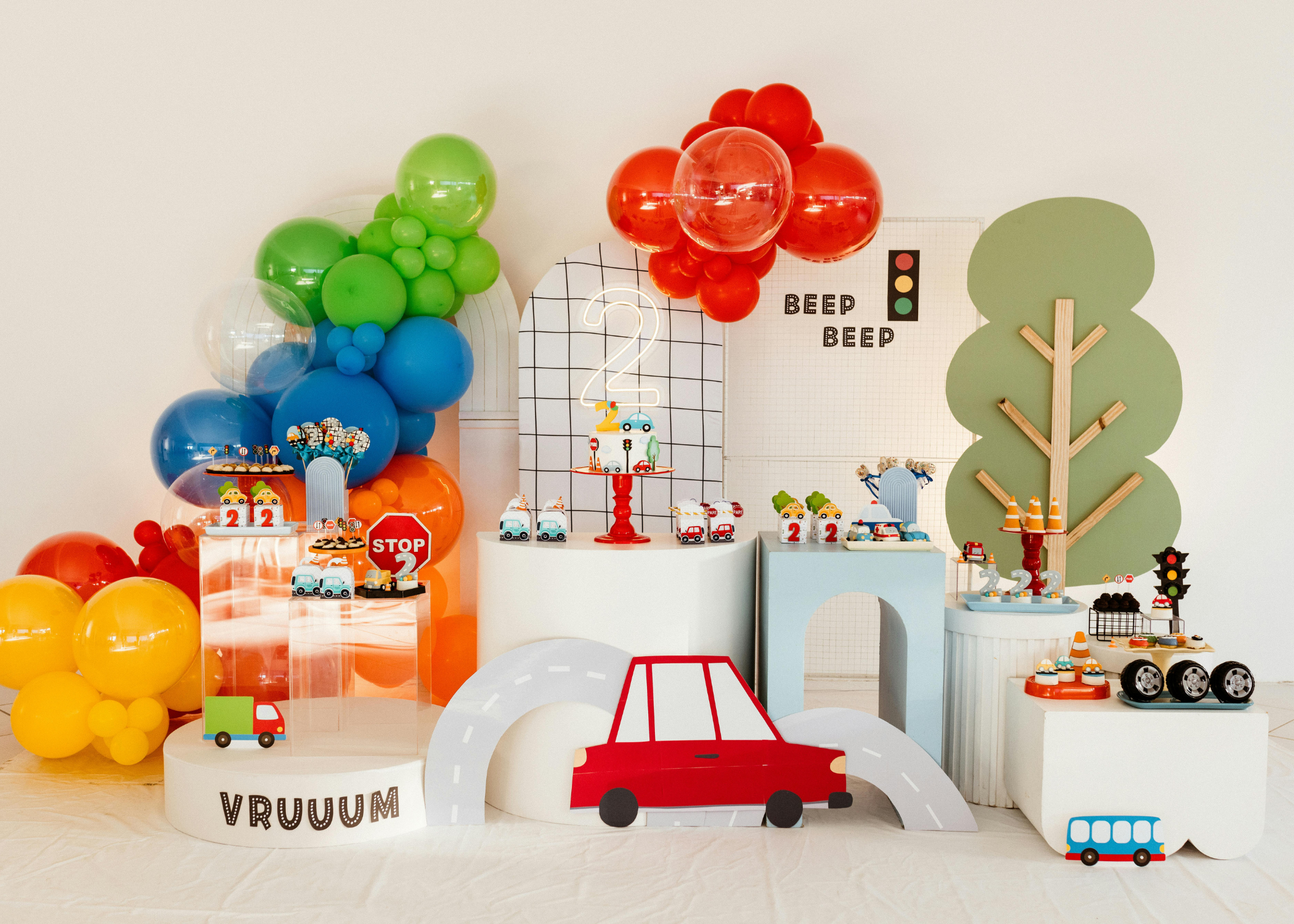 Colorful birthday party setup with balloons, toy cars, traffic signs, and traffic-themed decorations on a table and backdrop.
