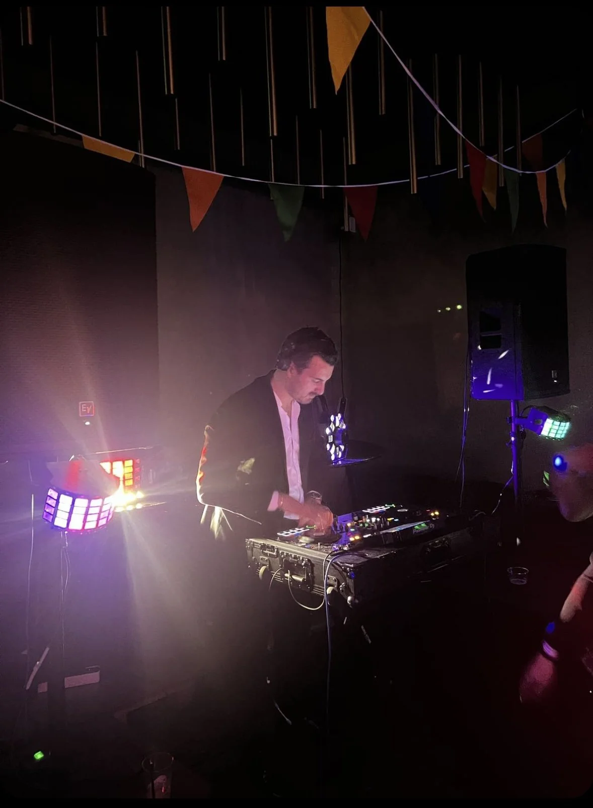 En DJ spiller musik ved en fest med farverige lys og pyntede flag.