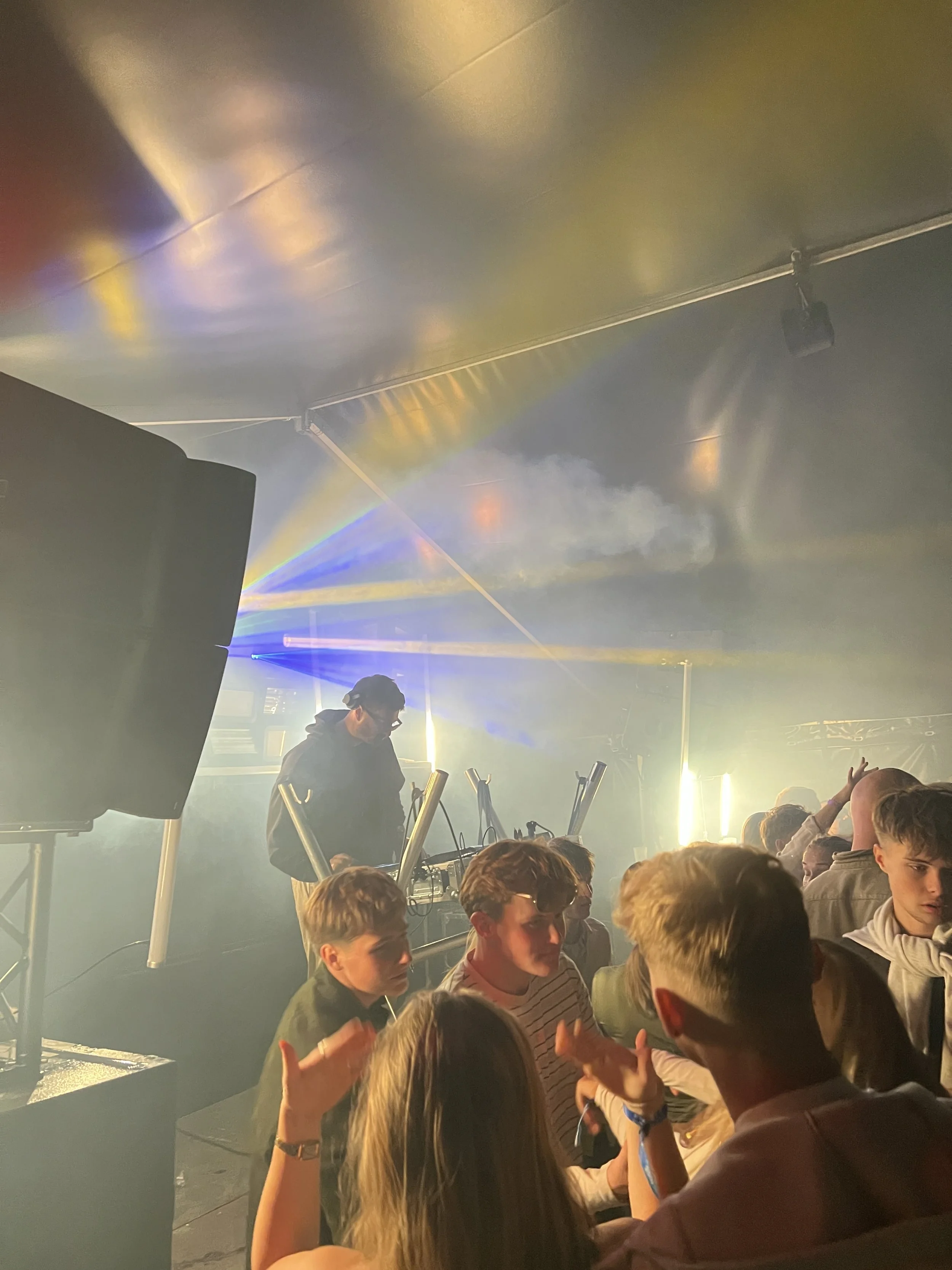 En DJ spiller musik til en gruppe unge mennesker ved et arrangement med farverige lys og skyer af røg.