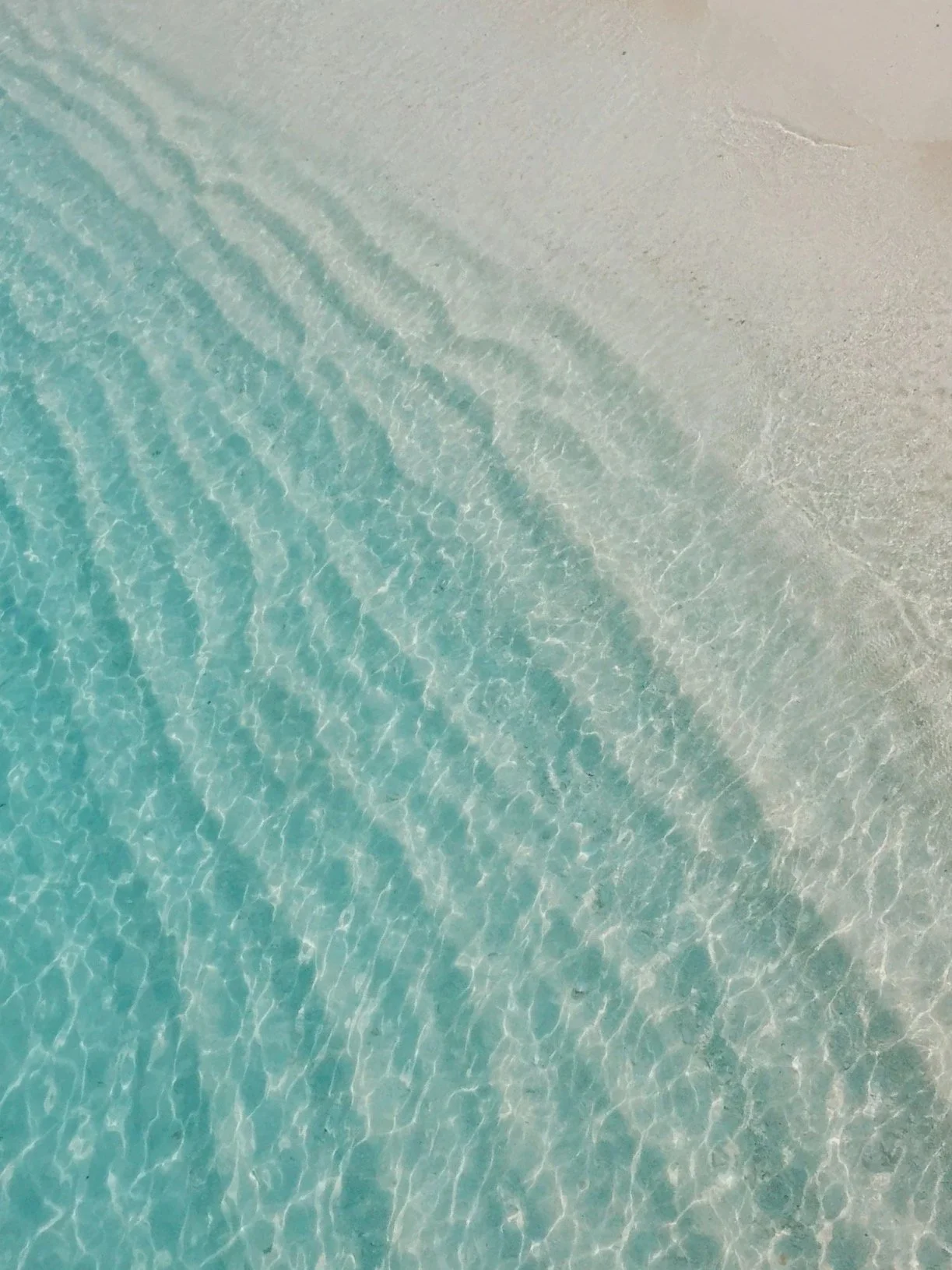 Close-up of clear turquoise water gently lapping onto a sandy beach.