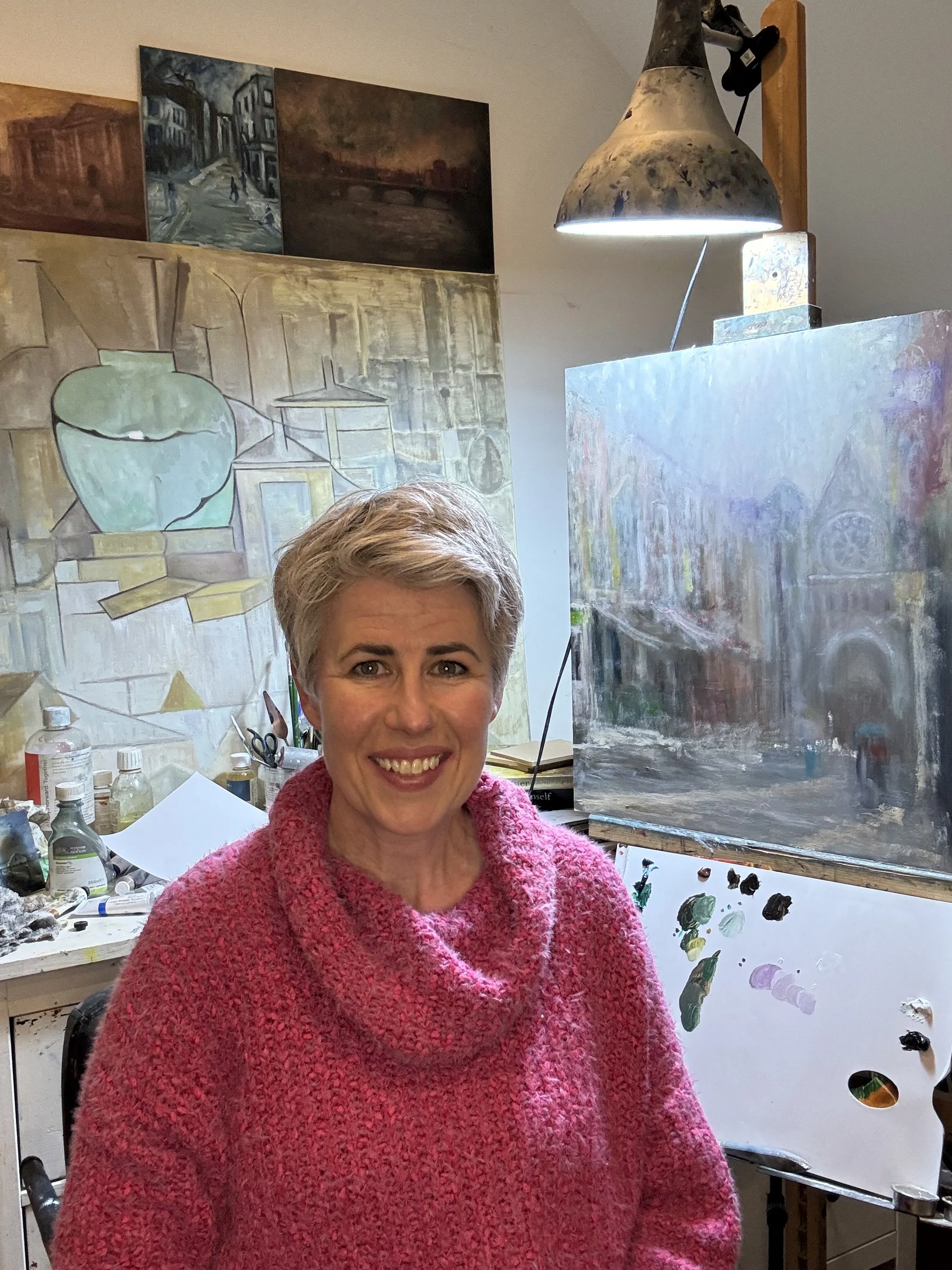Emily McCormack seated in her artist's studio, surrounded by paintings.