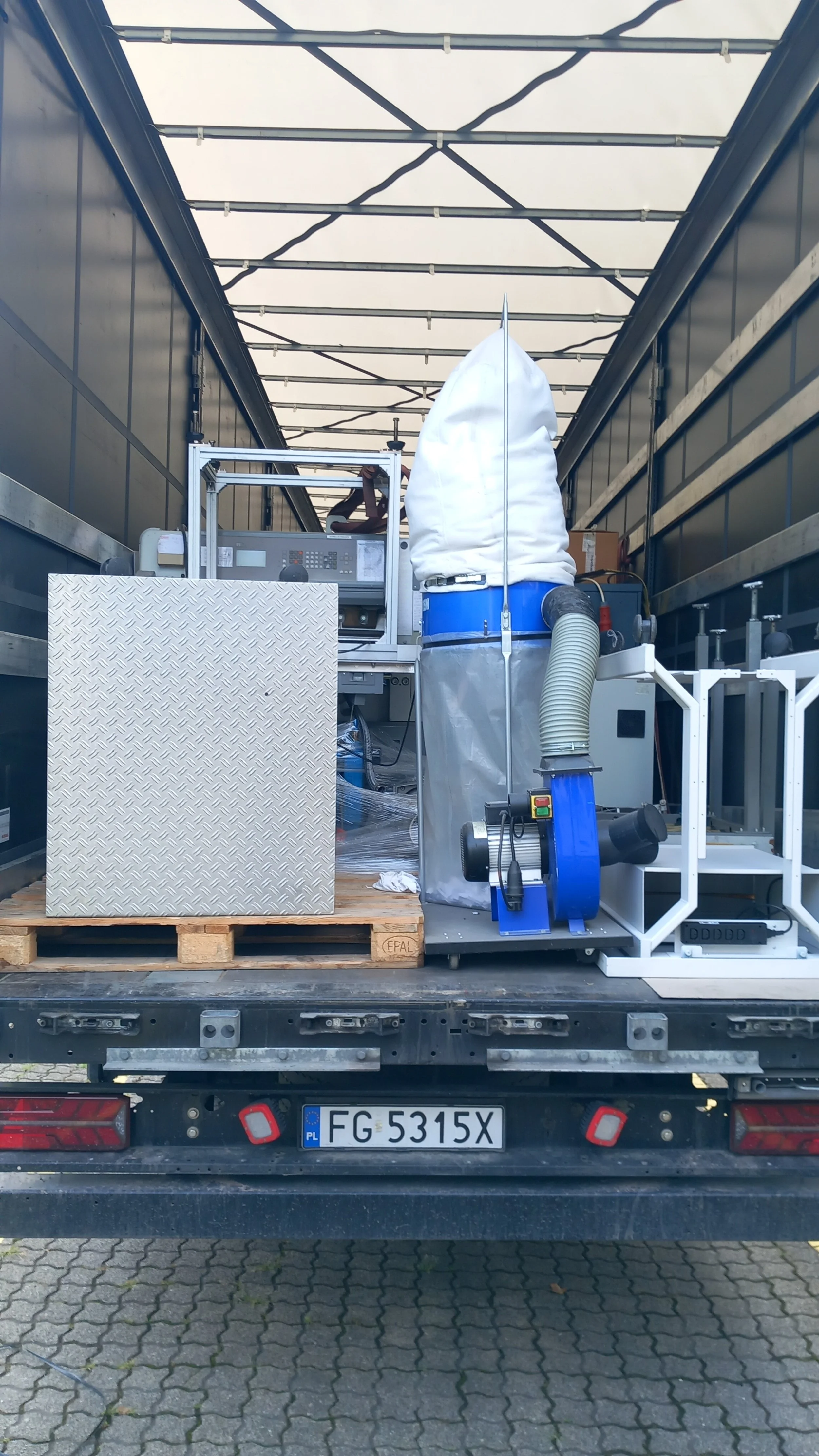 LKW-Ladefläche mit technischen Geräten, einer großen weißen Staubschutzhaube, einem blauen Filter, Schläuchen und elektronischen Steuerungen, bereit für den Transport.