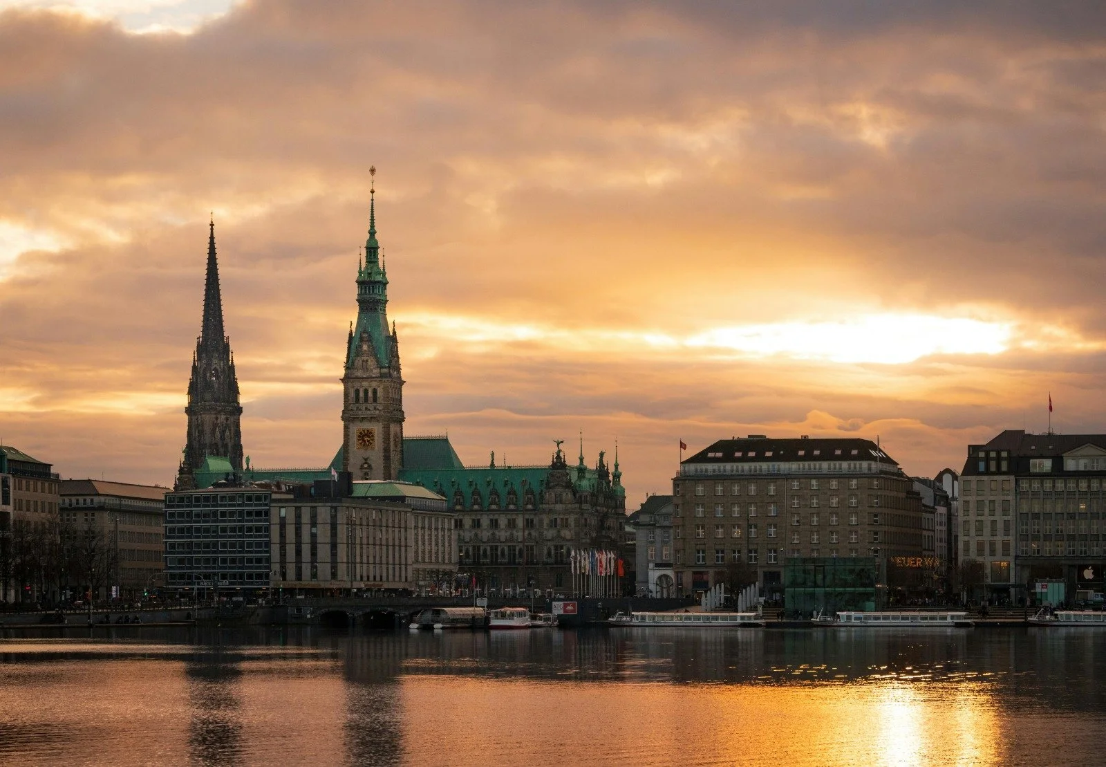 Stadt Panorama bei Sonnenuntergang mit Wasser im Vordergrund, historischer Kirche mit zwei hohen Türmen im Zentrum, moderne Gebäude im Vordergrund.