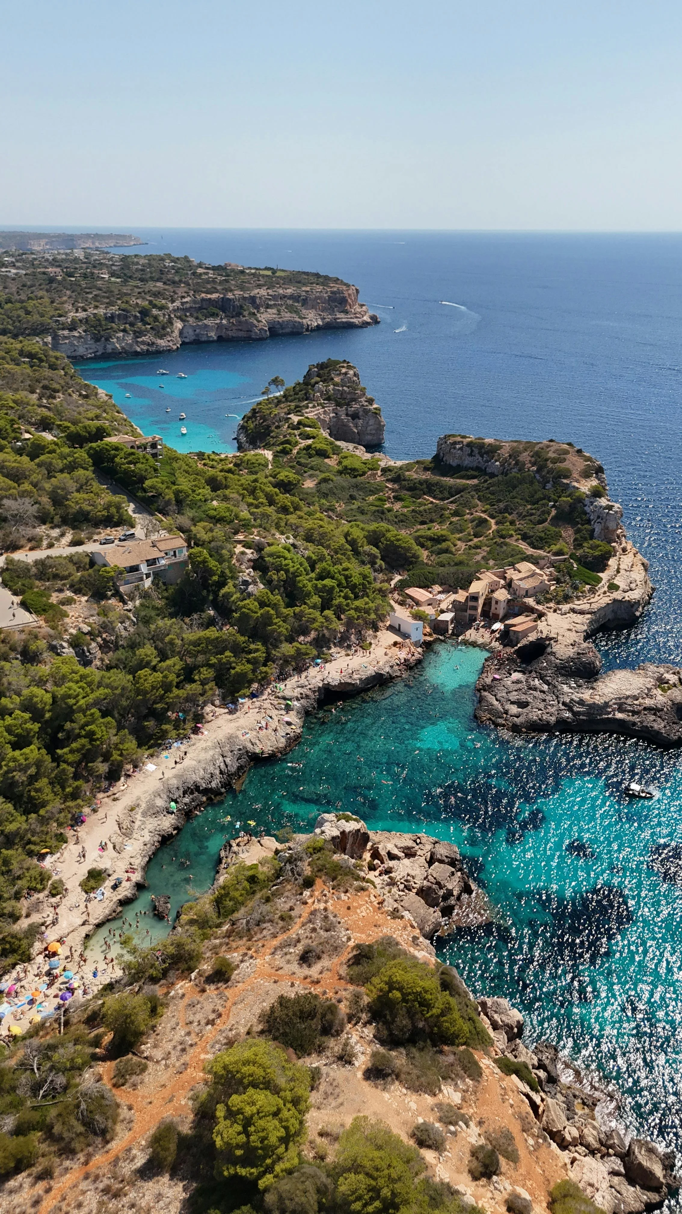 Luftaufnahme einer felsigen Küstenlinie mit kleinen Stränden, grünen Bäumen und azurblauem Wasser im Mittelmeer, mit Booten und versteckten Buchten