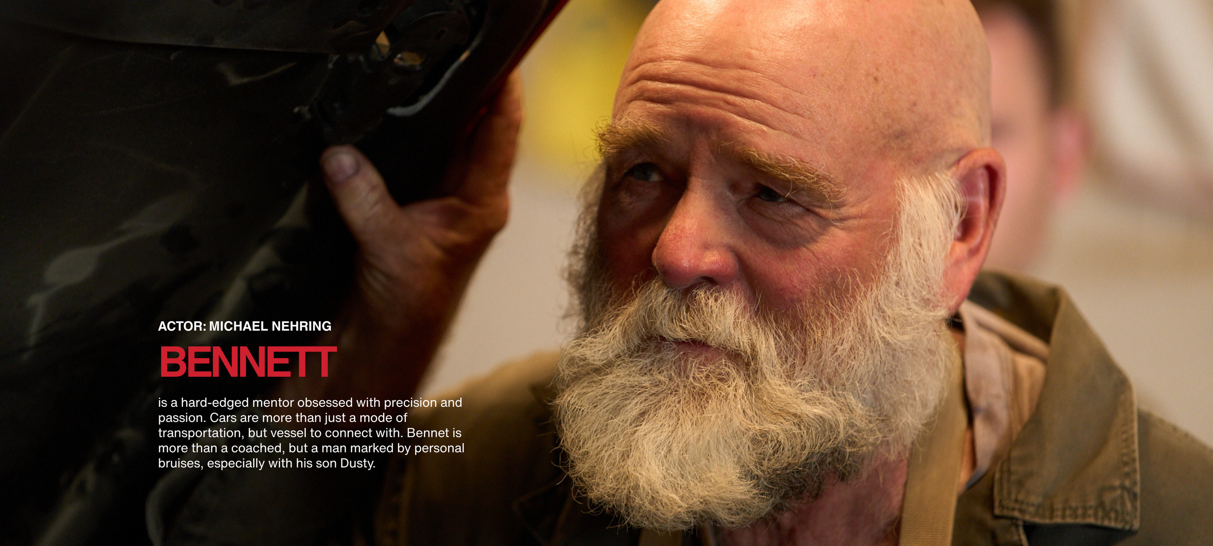 Close-up of an older man with a full white beard looking to the side, with a focused expression. The background is blurred.