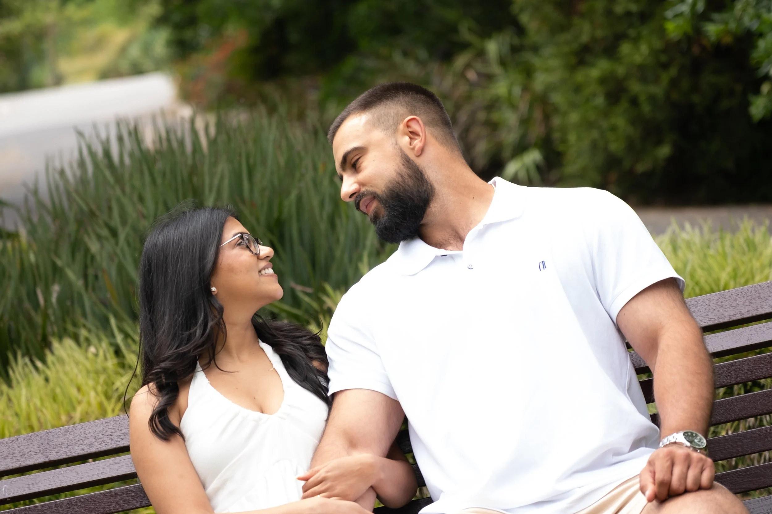A couple sitting on a park bench, gazing at each other and smiling.