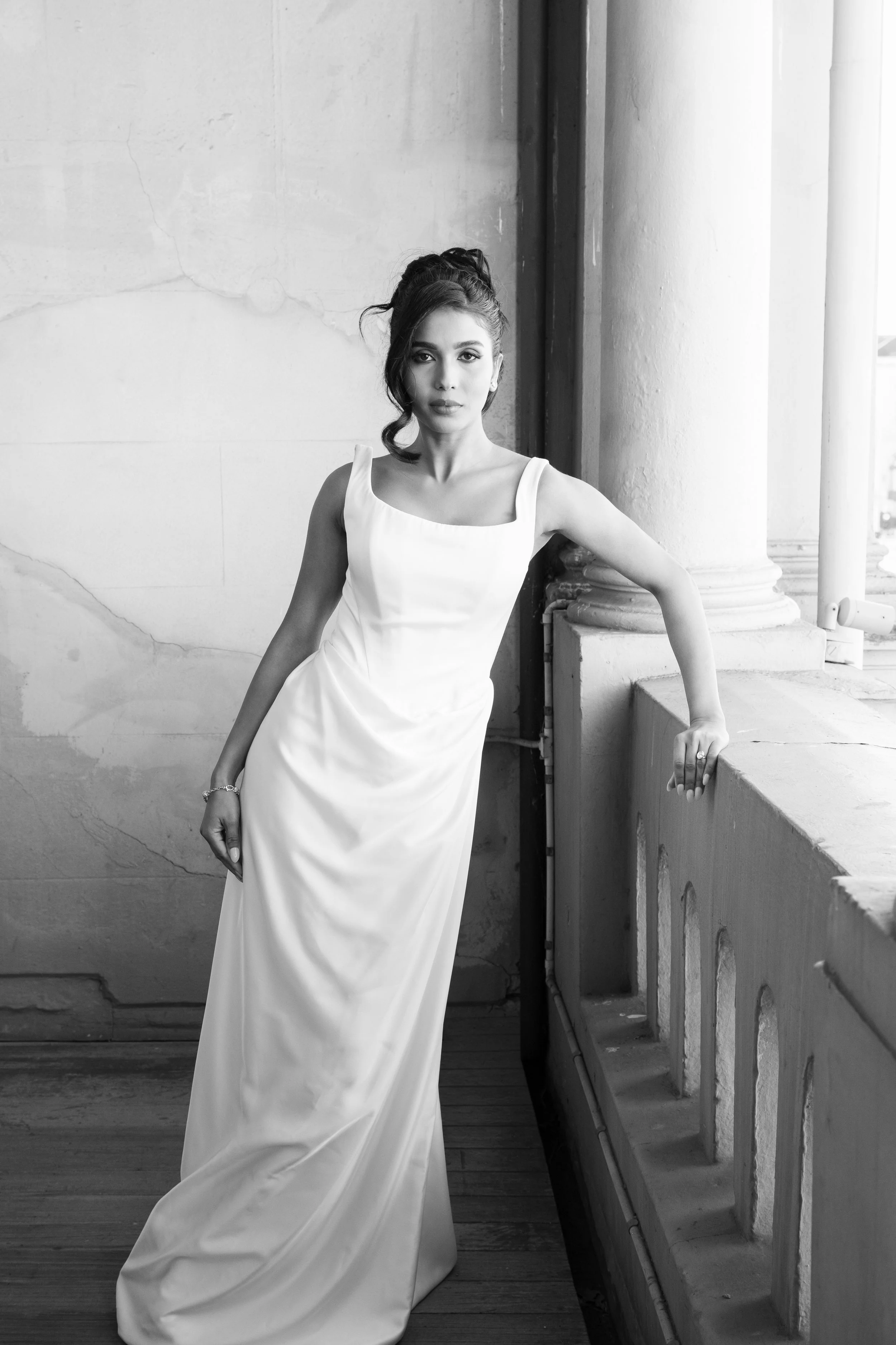 A woman in a white dress posing by a concrete railing indoors.