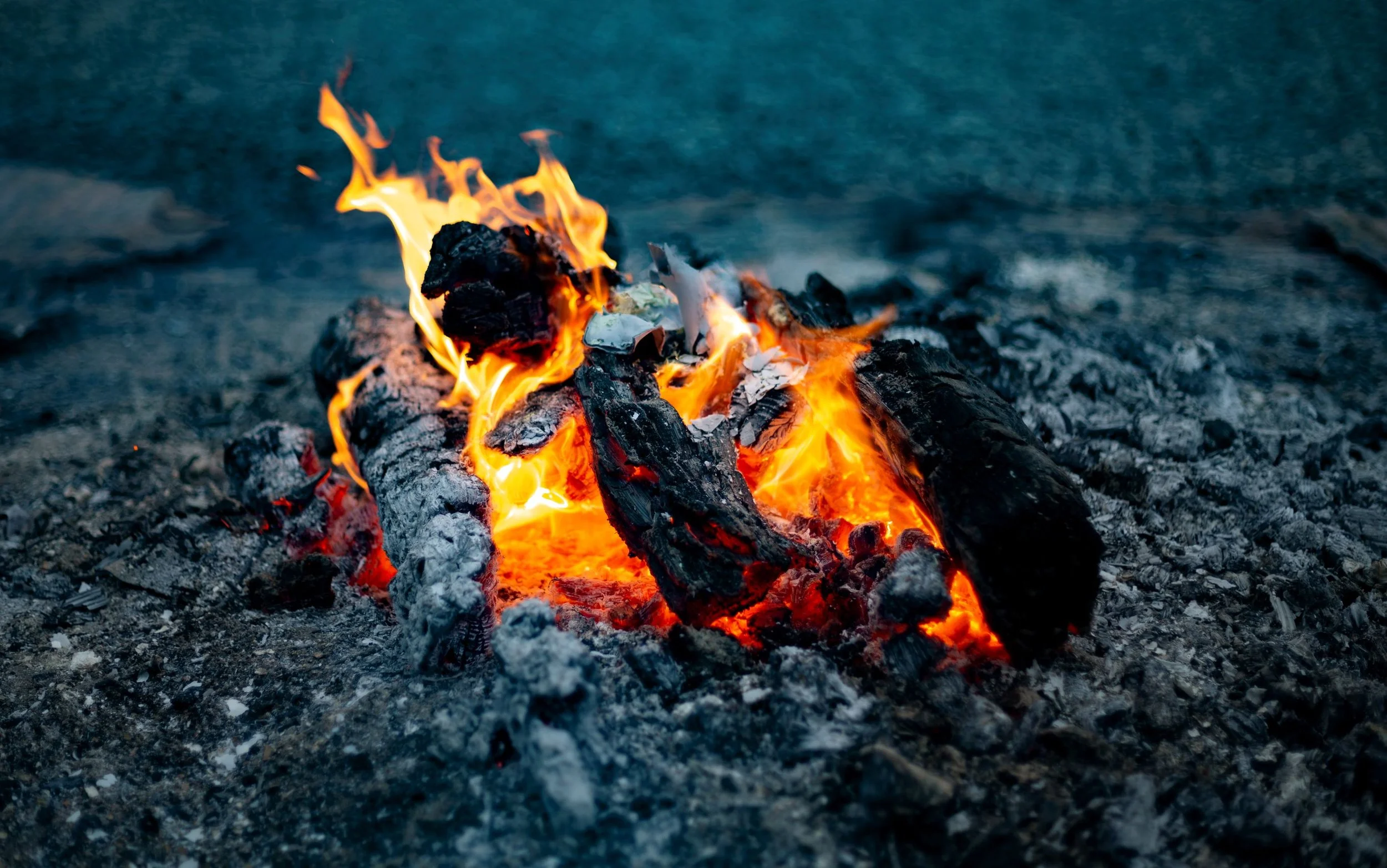 A small campfire with burning logs and bright orange flames on a gravel surface.