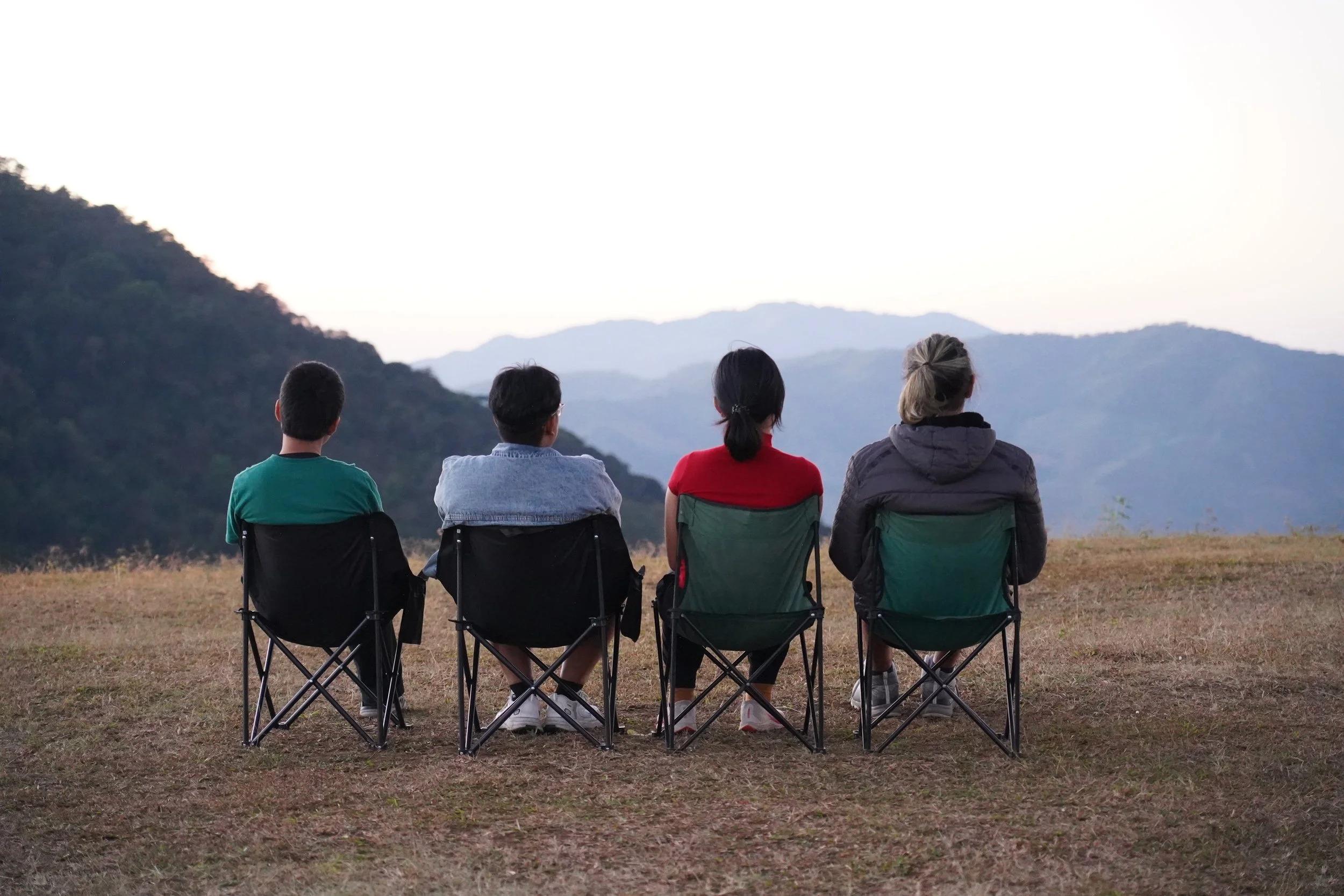 Four people sitting in camping chairs and watching a mountain sunset.