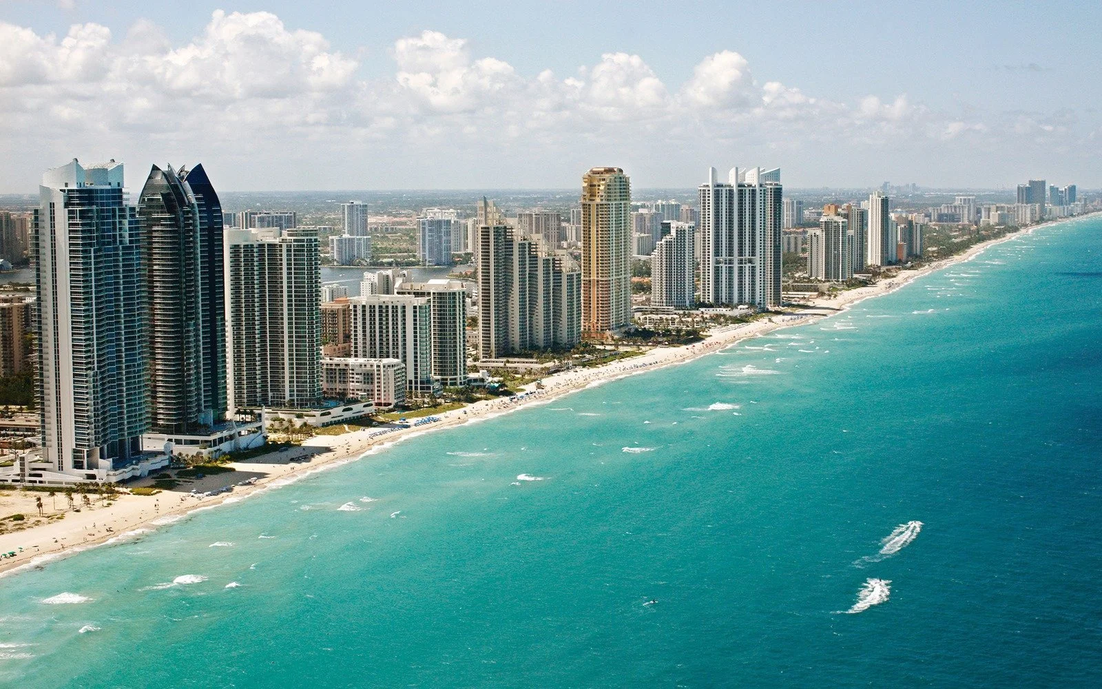 Aerial view of a coastline with high-rise buildings along the beach and an ocean with small waves.