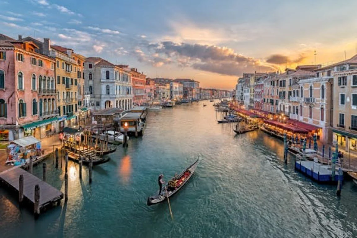 Colorful buildings lining a waterway at sunset with boats and gondolas docked along the sides.