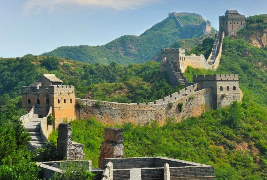 Long section of the Great Wall of China stretching over green hills under a partly cloudy sky.