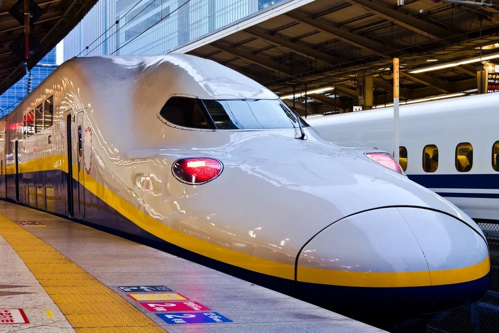 A modern high-speed train at a train station, with a sleek and streamlined design, white and yellow exterior, and reflective windows.