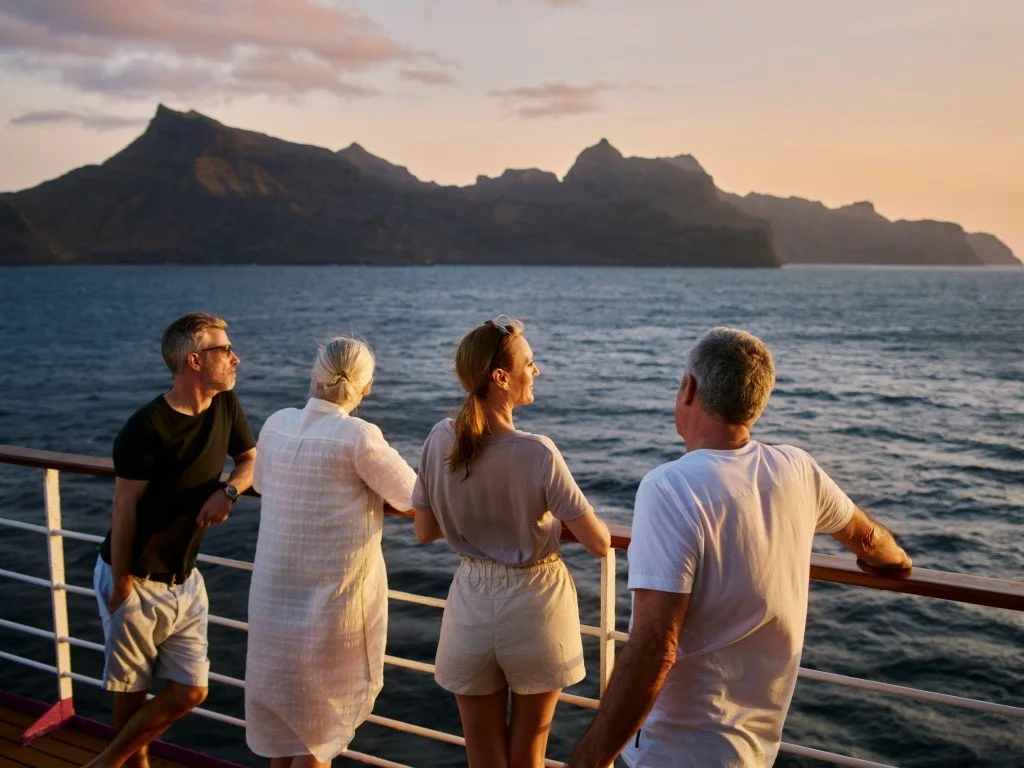 Four people on a boat deck looking at a sunset over mountains and water.