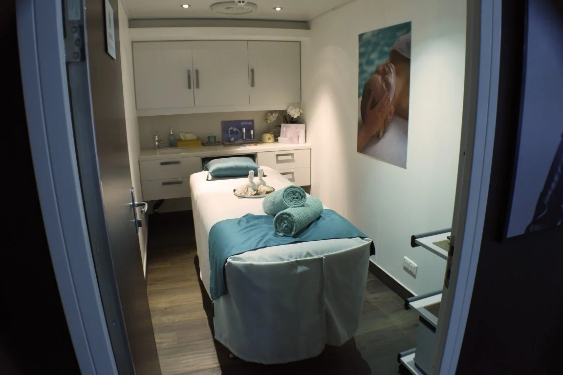 A massage therapy room with a massage table covered in teal sheets and towels, flower decorations, and a wall photo of a woman relaxing while getting a massage.