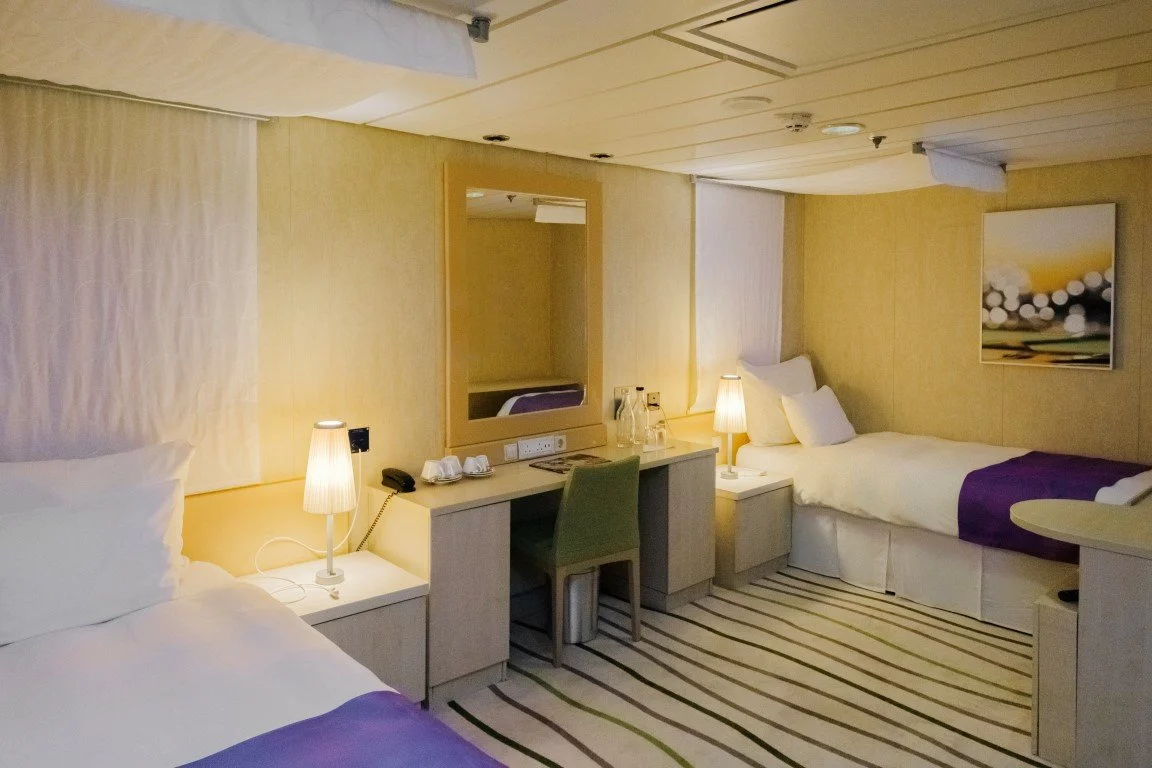 Hotel room with two beds, bedside lamps, a desk with a mirror, and artwork on the wall.