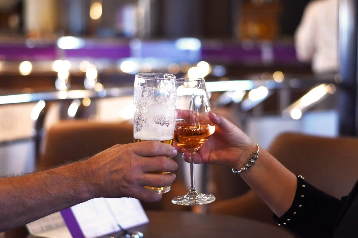 Two people are clinking glasses, one with beer and the other with rosé wine, in a restaurant or bar setting.