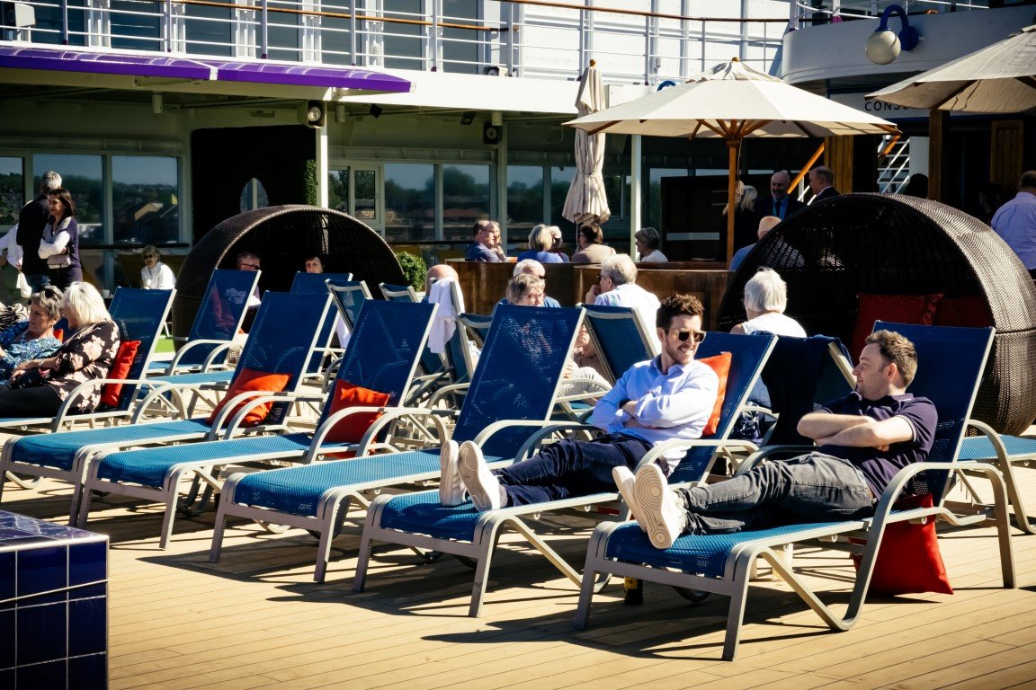 People lounging on deck chairs with umbrellas on a cruise ship balcony.