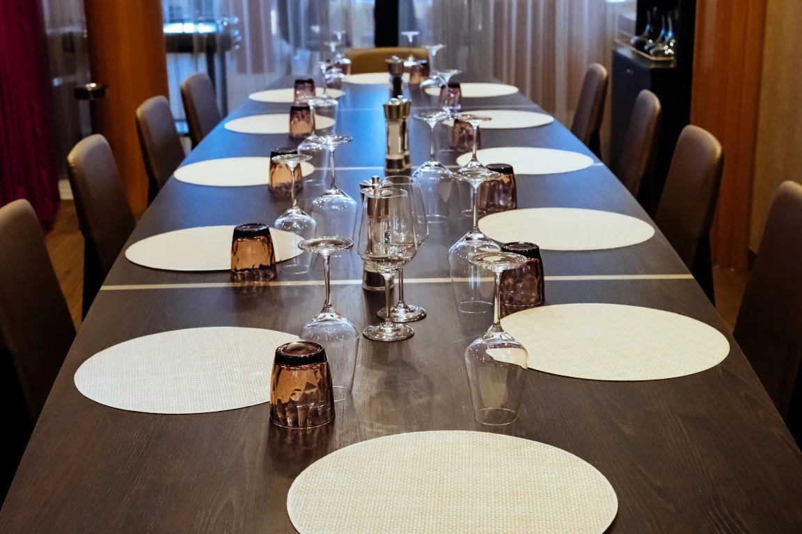 Empty dinner table set with glasses, cups, and white placemats in a restaurant dining room.