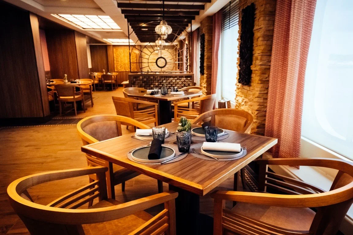 Empty restaurant dining area with wooden tables, chairs, and window curtains.
