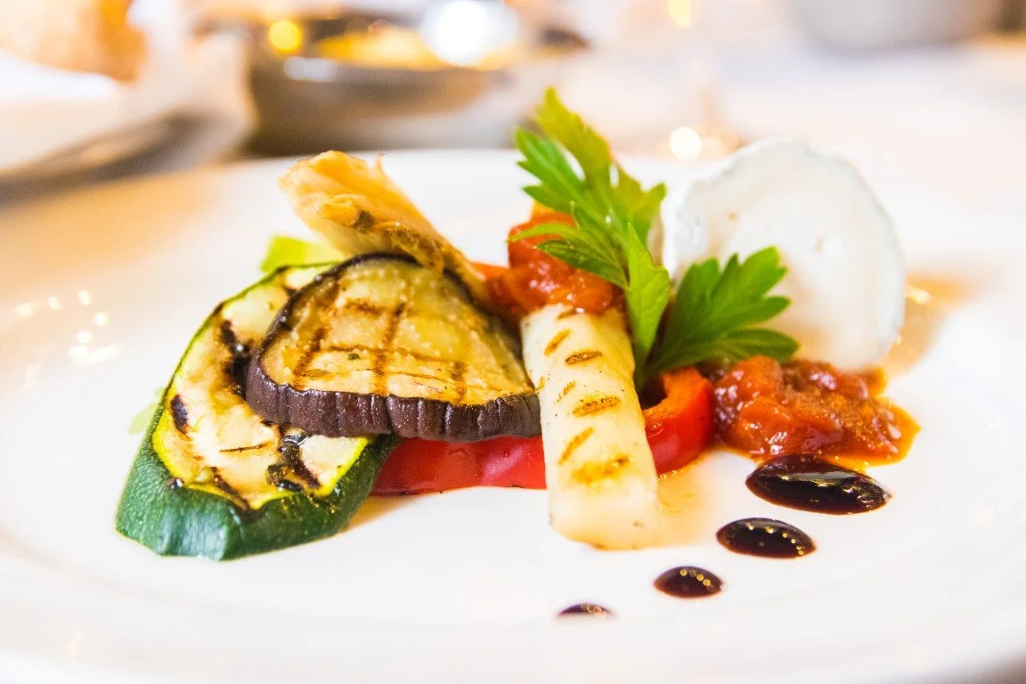 Grilled vegetables on a white plate with garnish and sauce