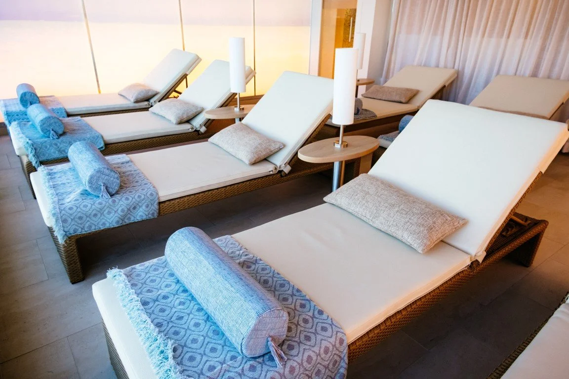 Multiple outdoor lounge chairs with pillows and towels, set in a relaxation area with side tables and lamps.