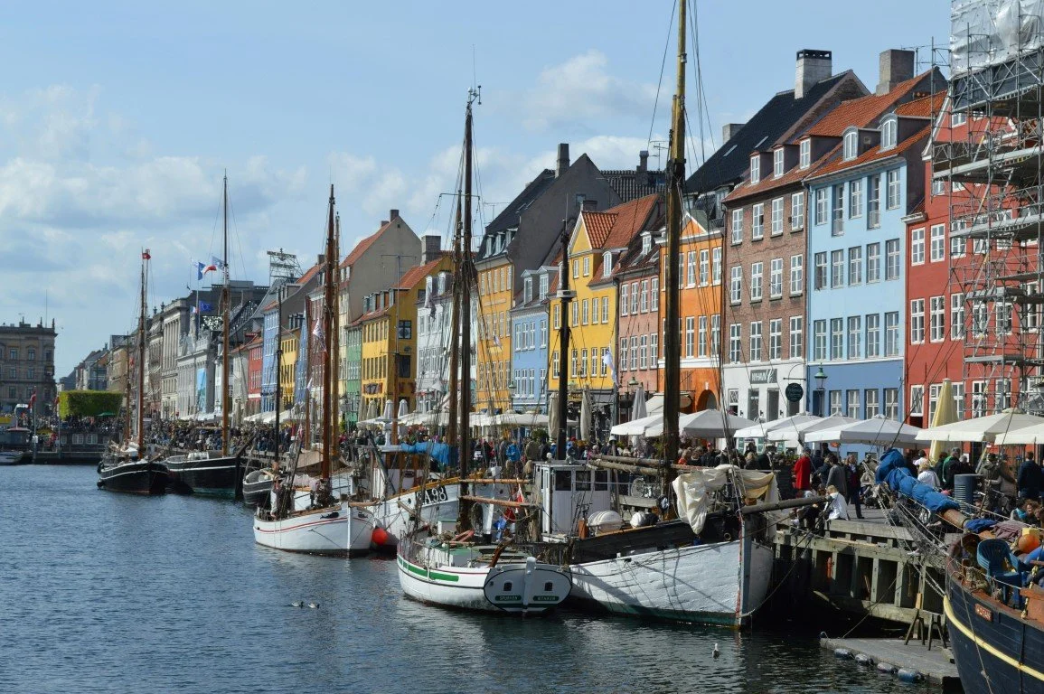 Colorful buildings along a canal with docked boats and people walking on the waterfront.