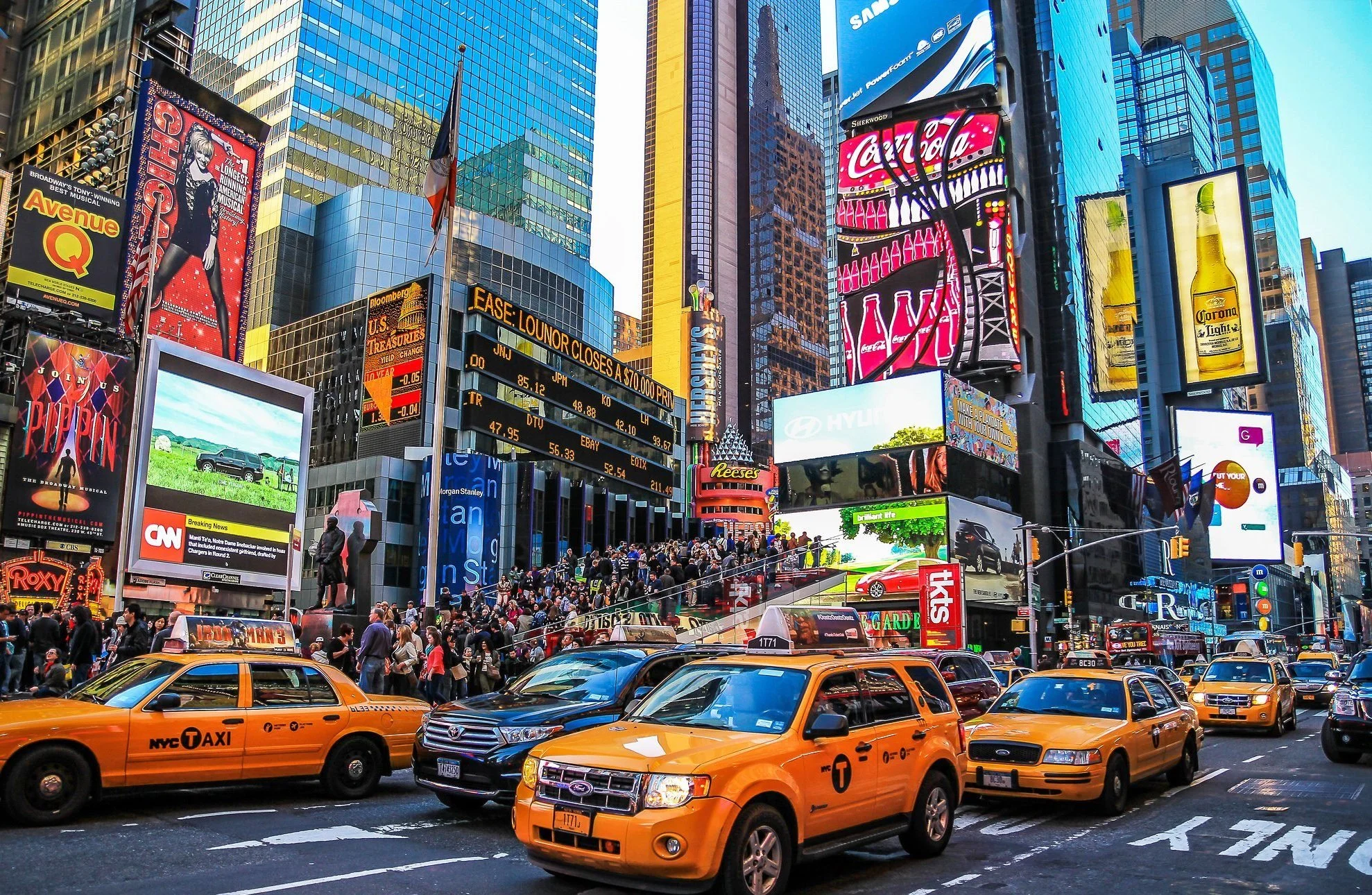 Times Square in New York City with yellow taxis, electronic billboards, and a crowd of people.