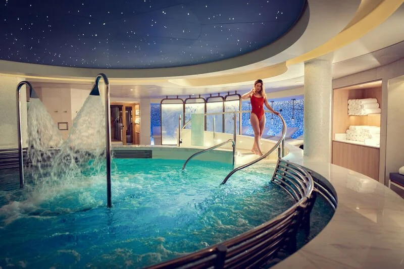 Luxury indoor spa with hot tub, waterfalls, and a woman in a red bathing suit.