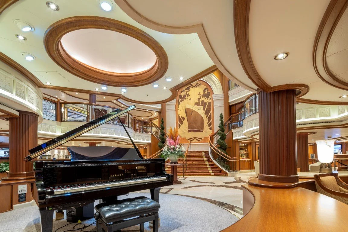 Lounge with a grand piano, floral arrangement, staircase, and wood-paneled columns and walls.