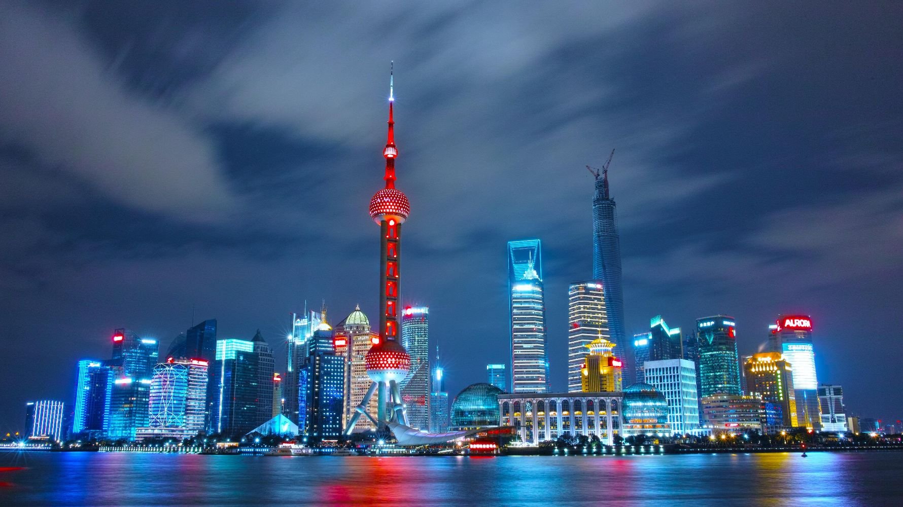 Night view of the illuminated Shanghai skyline with the Oriental Pearl Tower, Jin Mao Tower, Shanghai Tower, and other high-rise buildings reflected on the Huangpu River.