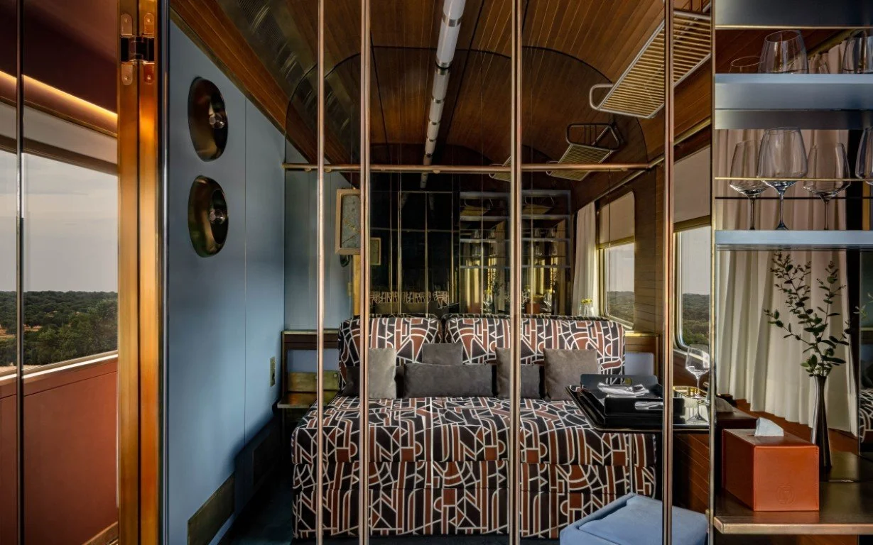 Cozy lounge area with patterned sofa, decorative pillows, and a small table with a tray, overlooking a scenic outdoor view through windows.