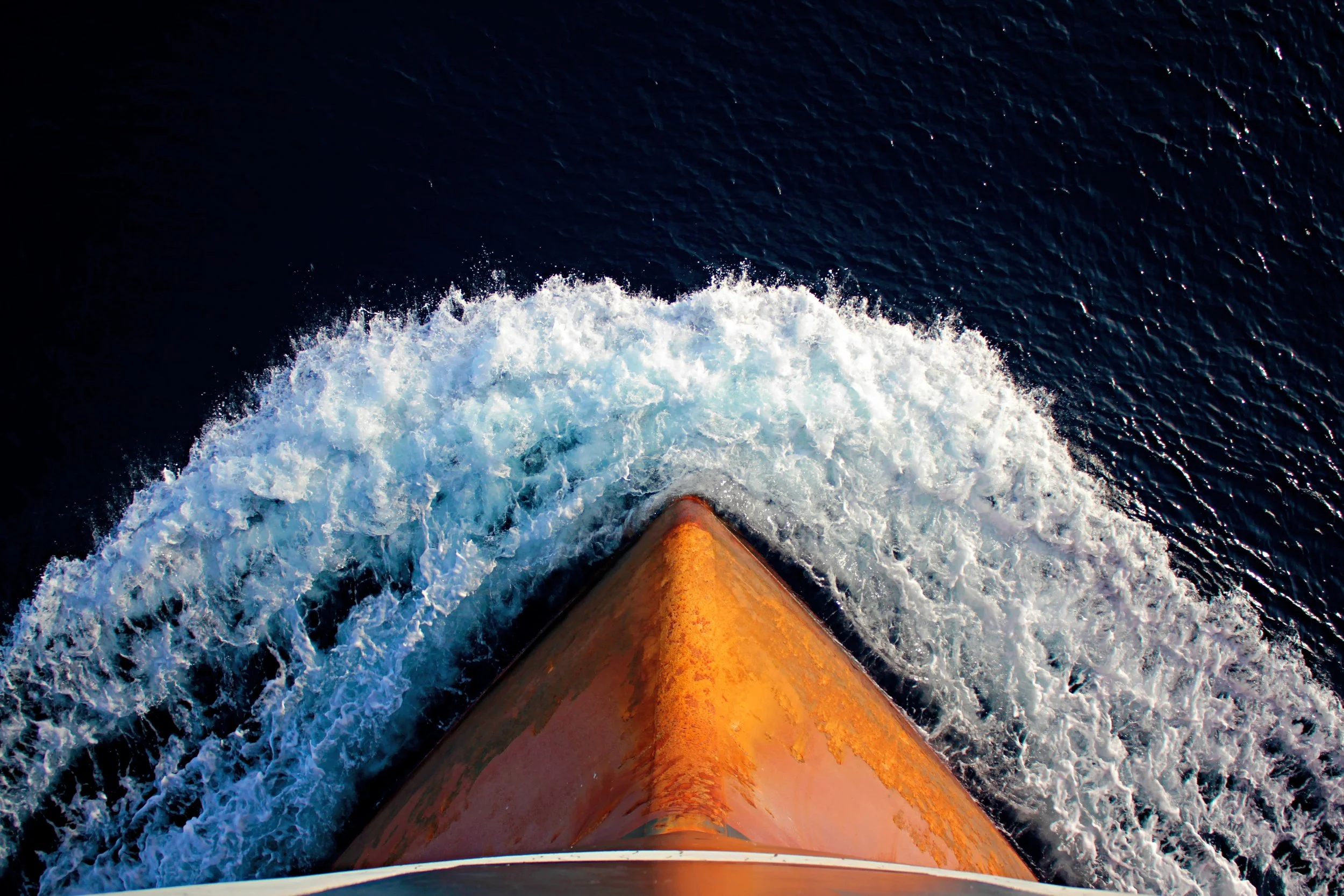 Aerial view of a ship's bow cutting through the water and creating waves.