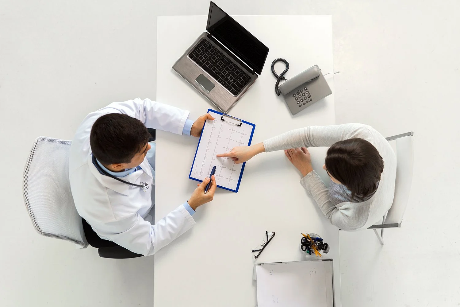 A doctor and a patient review an electrocardiogram (ECG) on a clipboard during a consultation in a medical office.