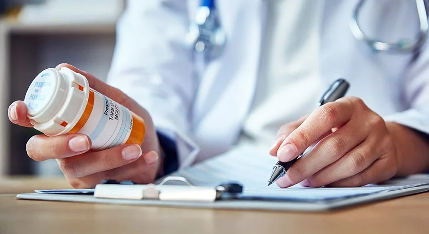 A healthcare professional holding a prescription medication bottle and writing on a medical chart.